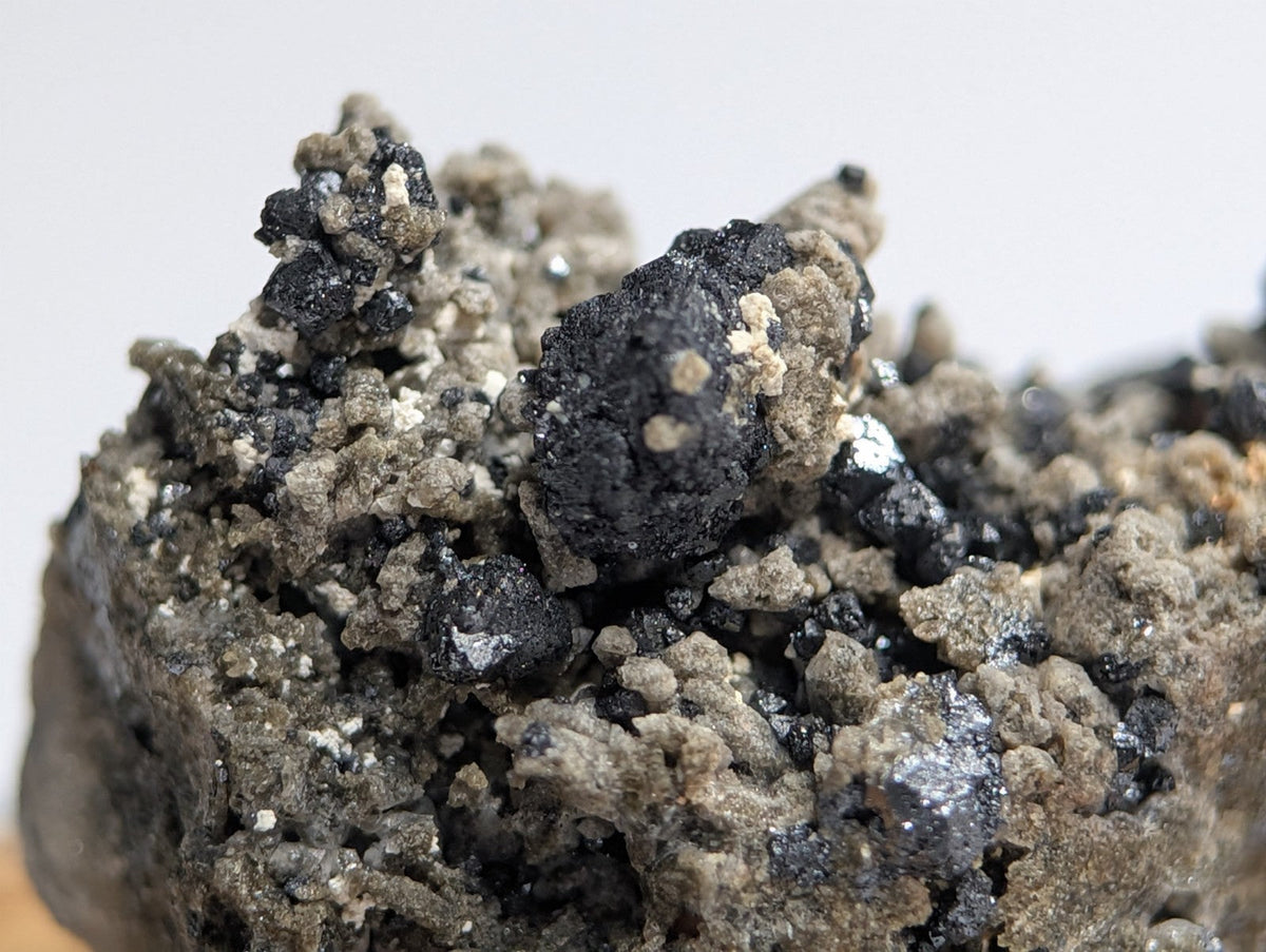 A rugged, textured mineral specimen featuring dark black and grayish-brown crystalline formations with scattered metallic sheen.