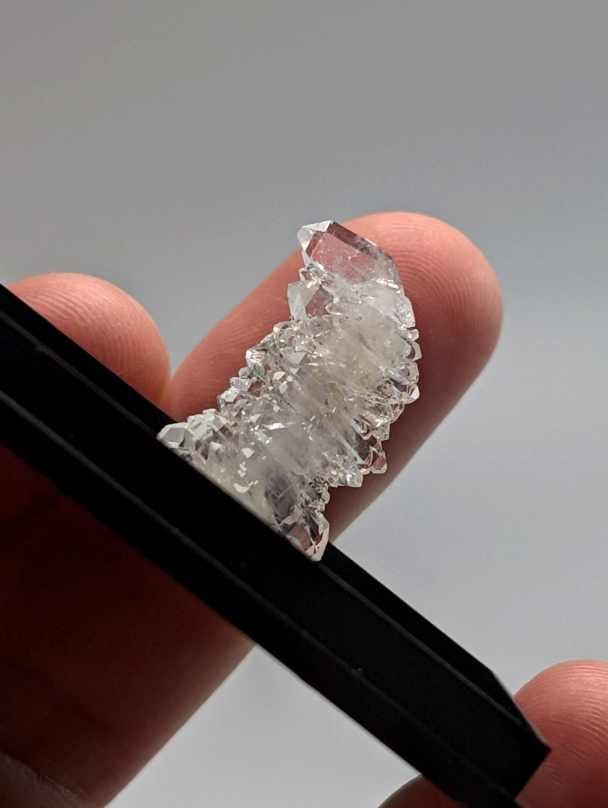 A clear, faceted quartz crystal cluster held delicately between fingers and a black tool.