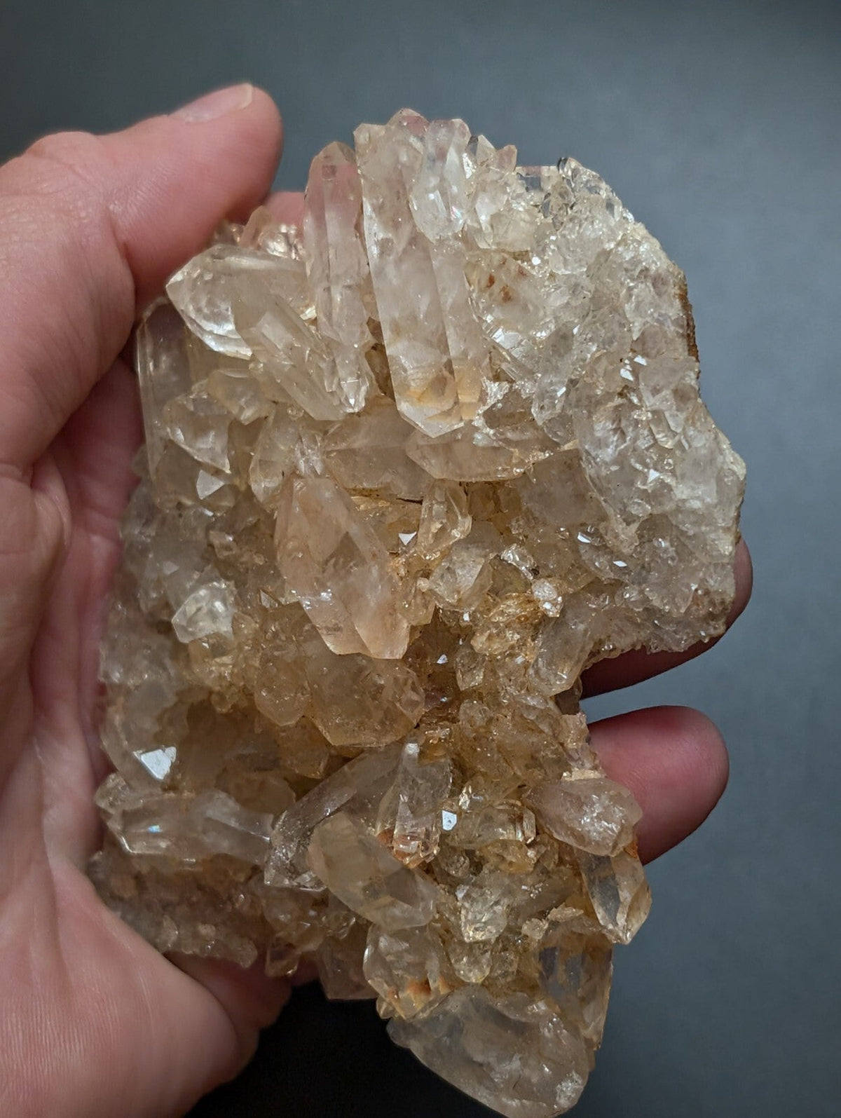 A hand holds a cluster of translucent, amber-hued quartz crystals with sharp, faceted edges and natural imperfections.