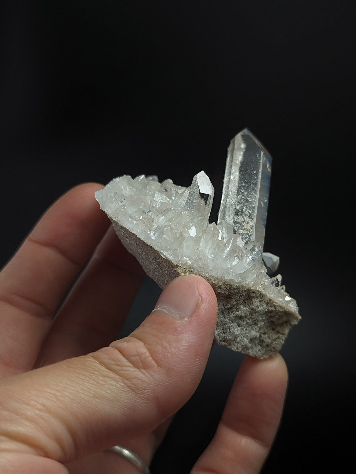 A translucent quartz crystal cluster with sharp, clear points emerging from a rough gray matrix.