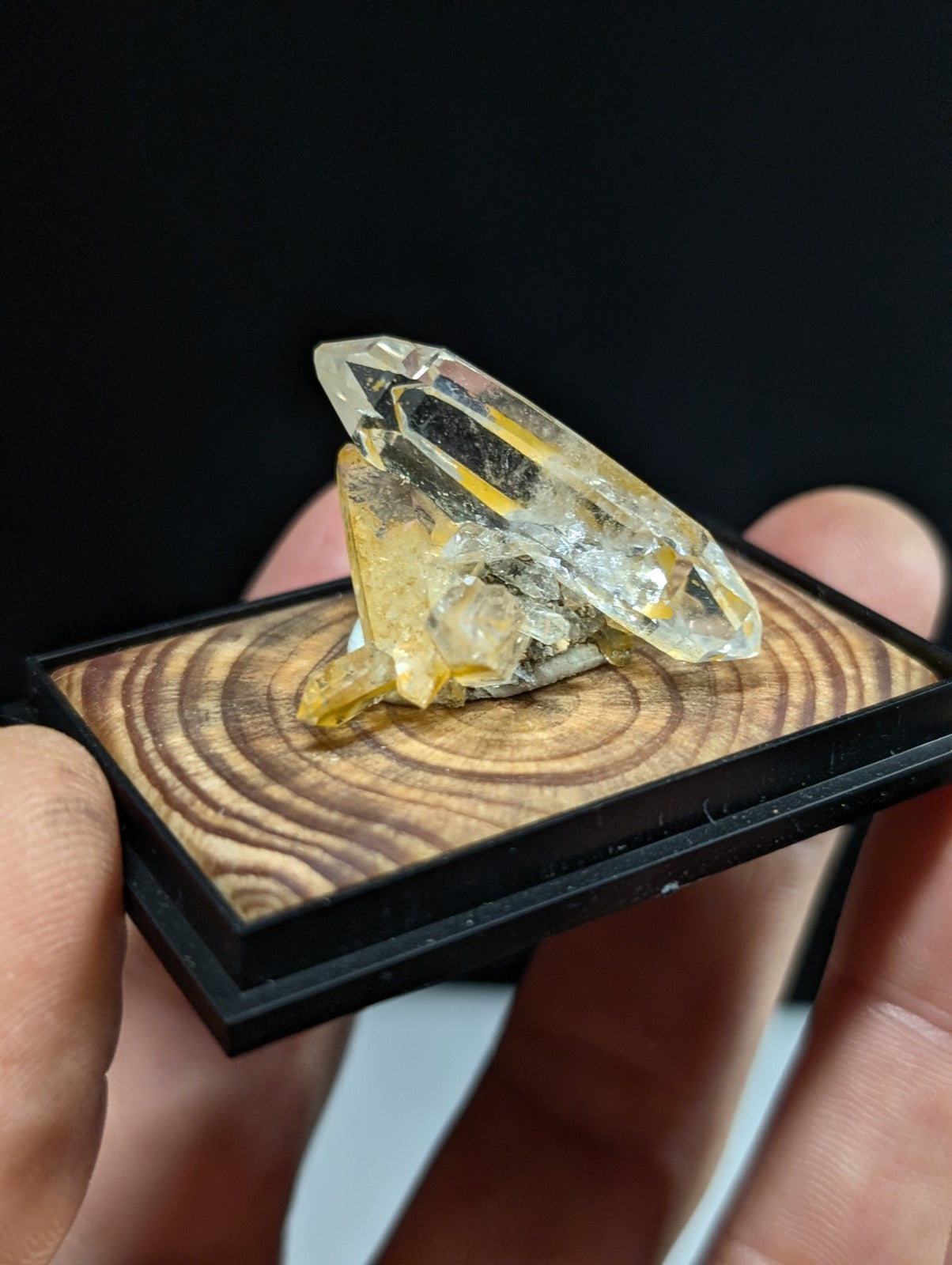 A translucent yellow crystal with sharp, faceted edges rests on a wooden display base.
