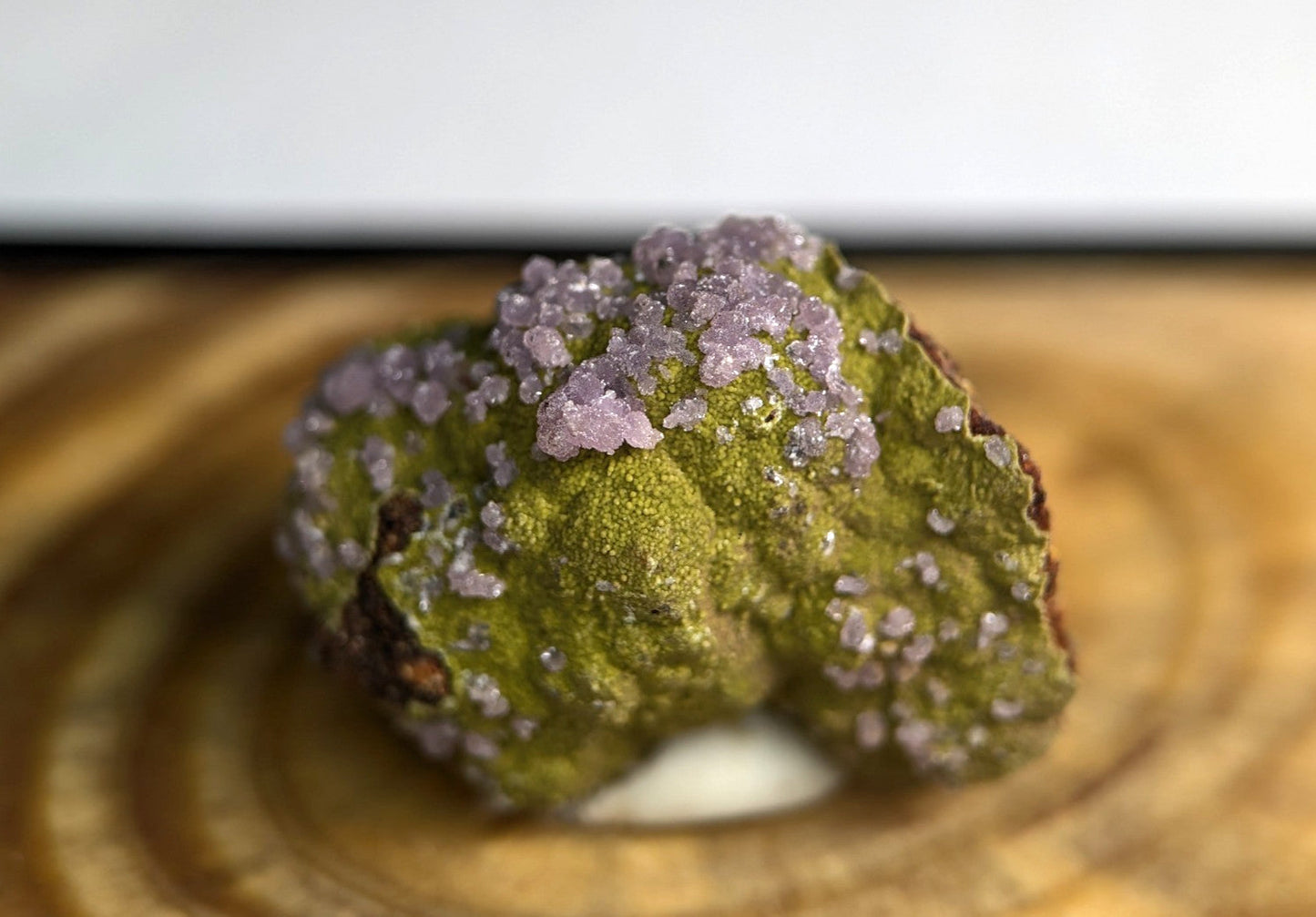 A vibrant green mineral specimen adorned with delicate, crystalline purple formations.
