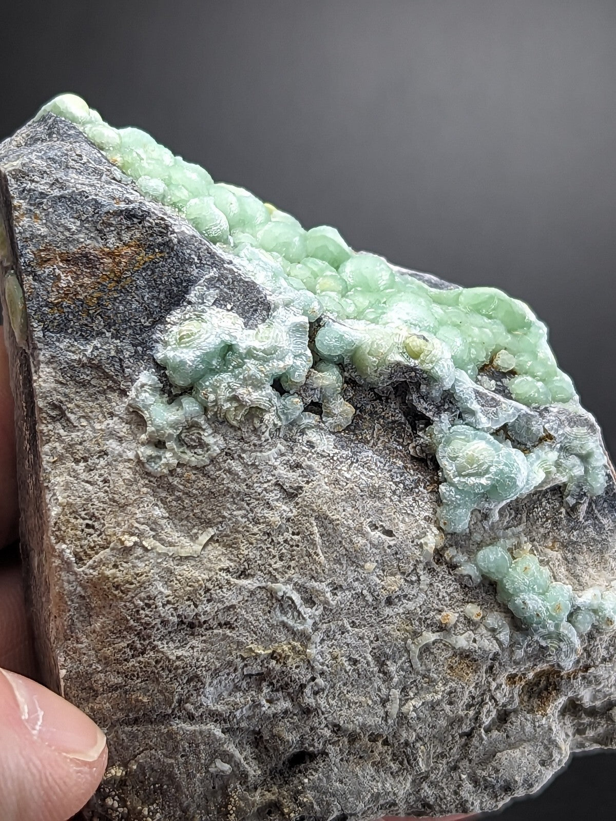 A rough, gray rock specimen featuring a cluster of translucent light green, bead-like crystals growing along its surface.