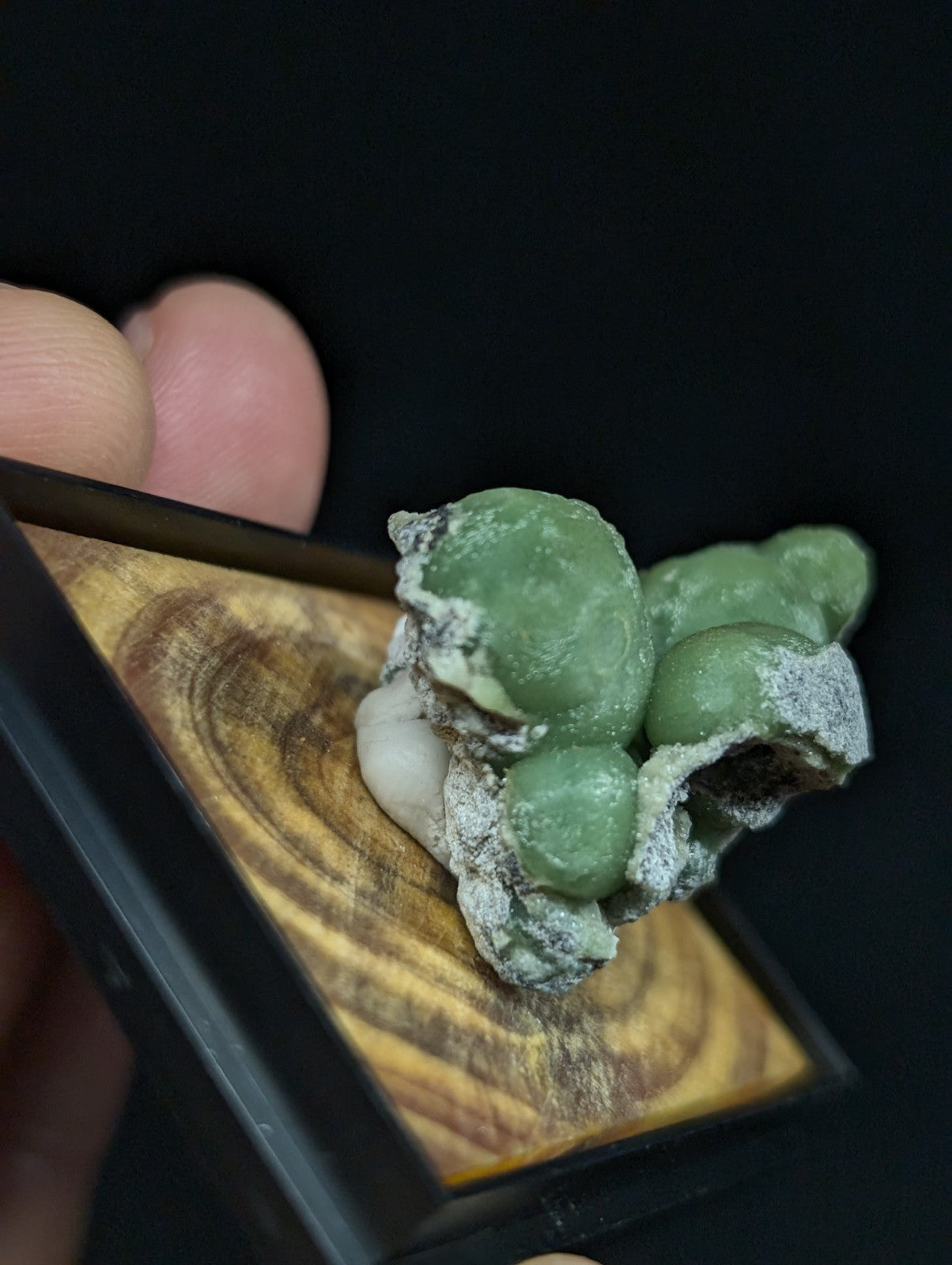 A cluster of translucent green and white mineral formations, resembling grapes or beads, rests on a wooden display base.