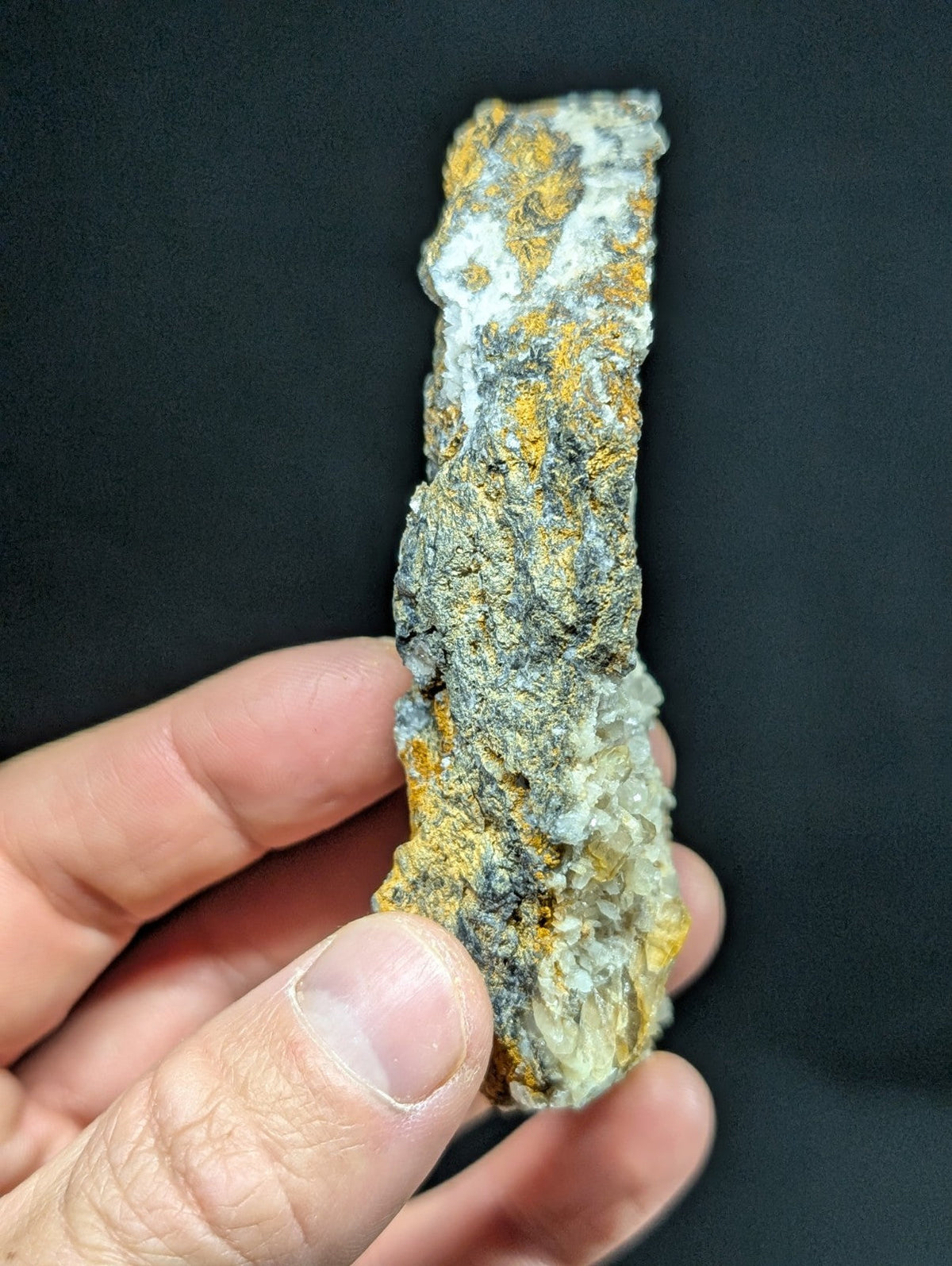 A rugged, irregularly shaped mineral specimen with a textured surface displaying patches of yellowish-orange and grayish-white hues.
