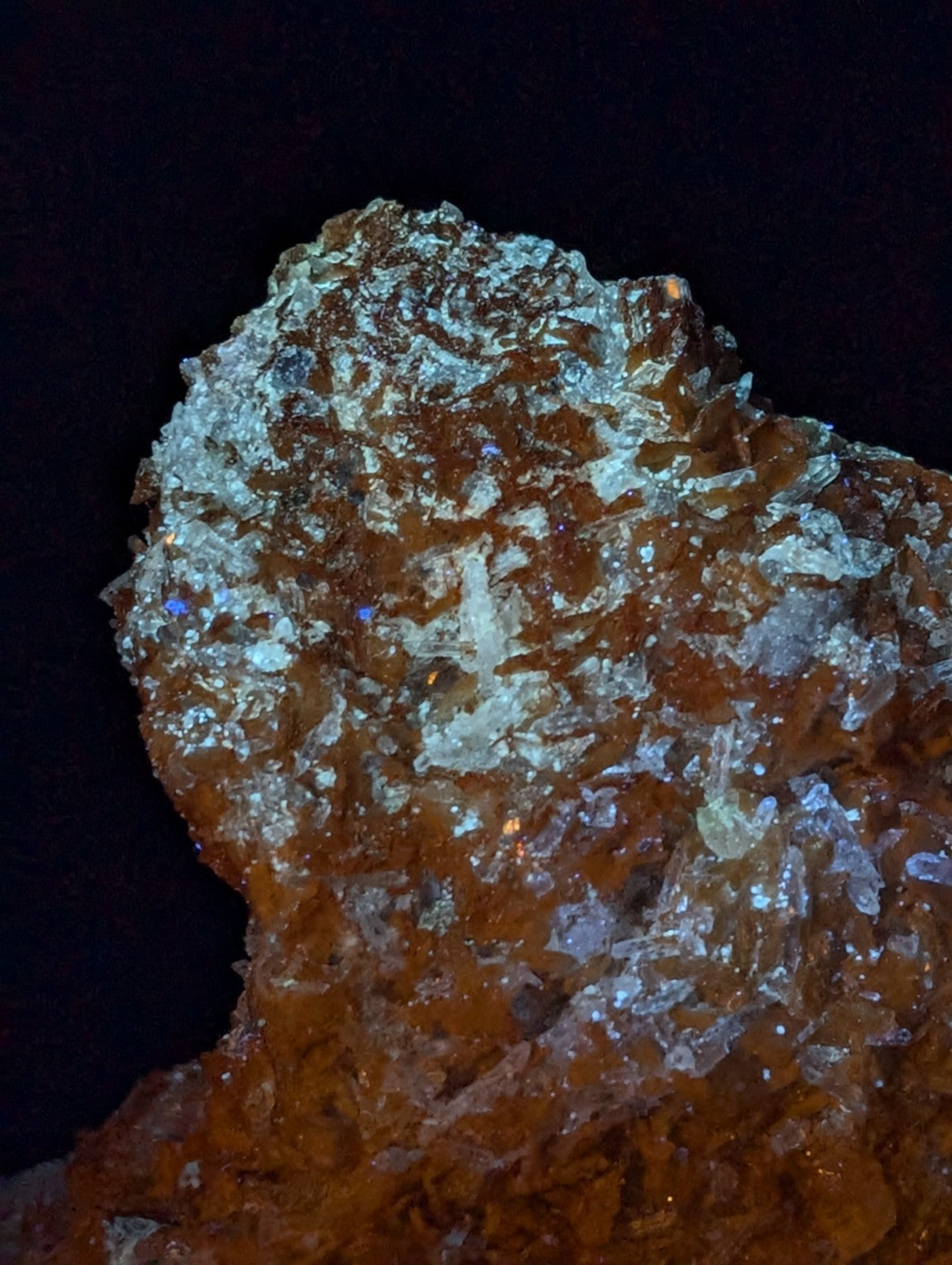 A rugged, translucent orange crystal formation with shimmering white and blue-tinged mineral inclusions.