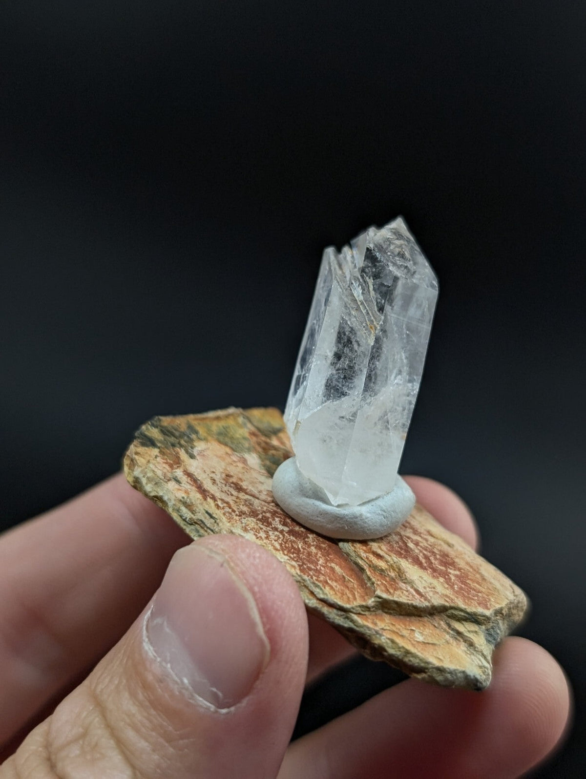 A clear, faceted quartz crystal mounted on a small white base and displayed atop a textured brown rock.