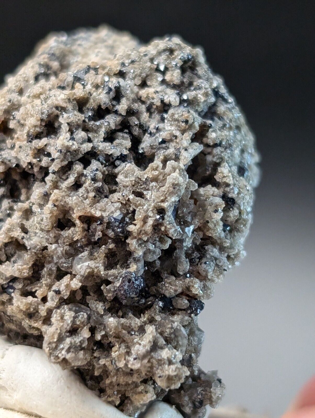 Rough, gray mineral formation with dark inclusions.