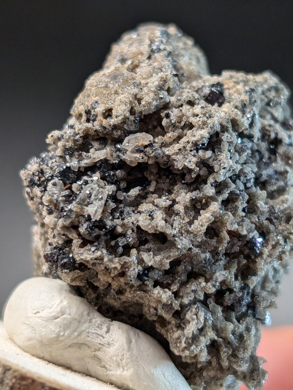 Rough, gray mineral specimen with dark inclusions.