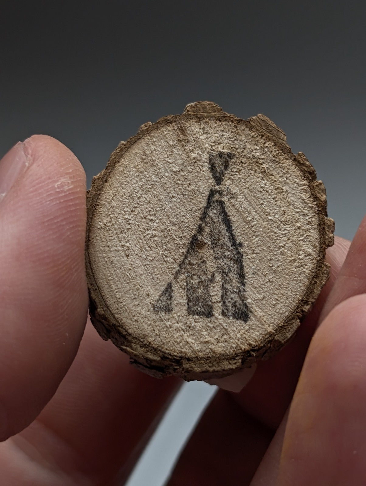 A rustic circular wooden slice with natural bark and charcoal burned teepee featuring clay-included quartz base