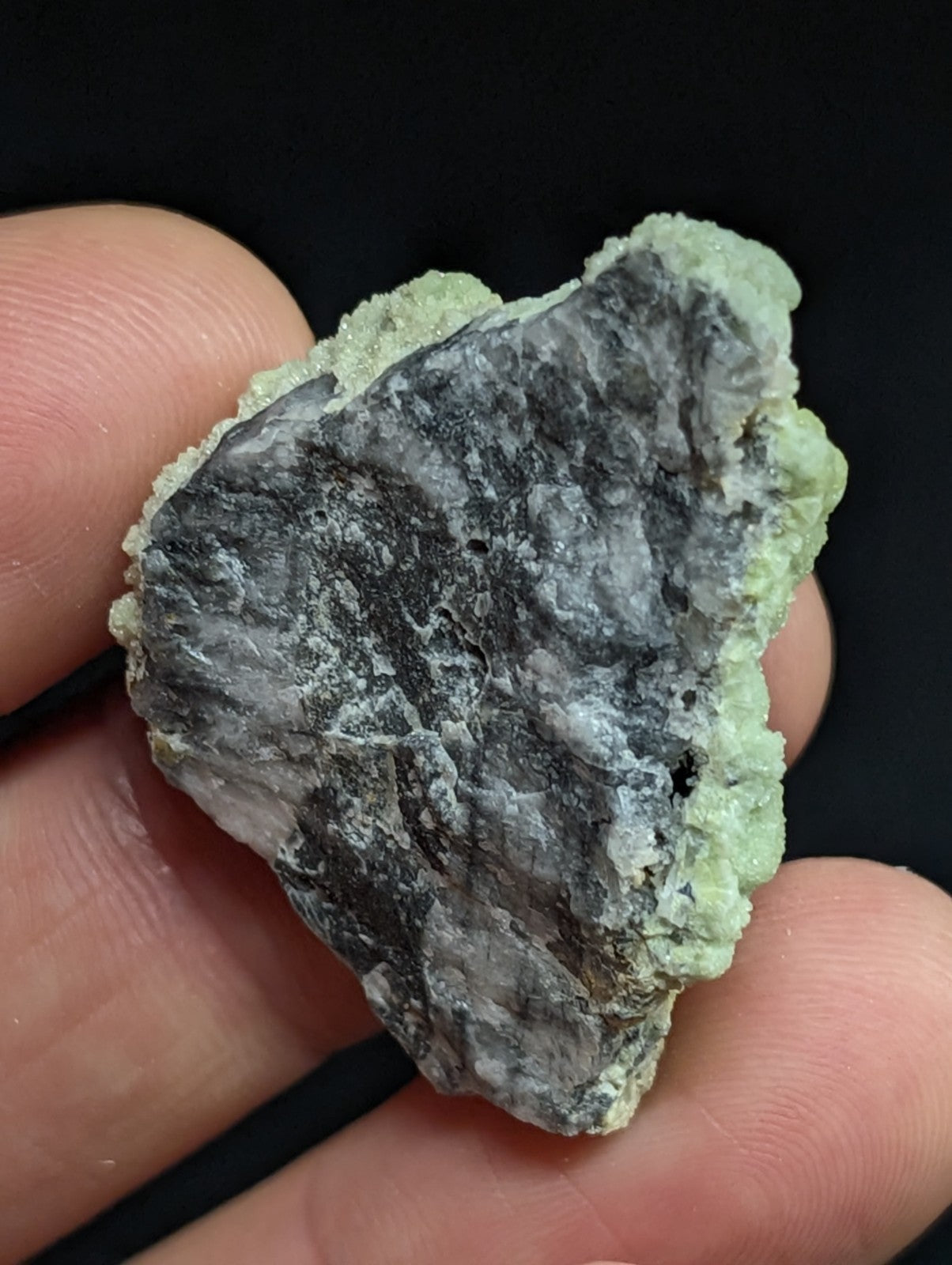 A rough, irregularly shaped mineral specimen with a dark gray core and light green crystalline matrix.