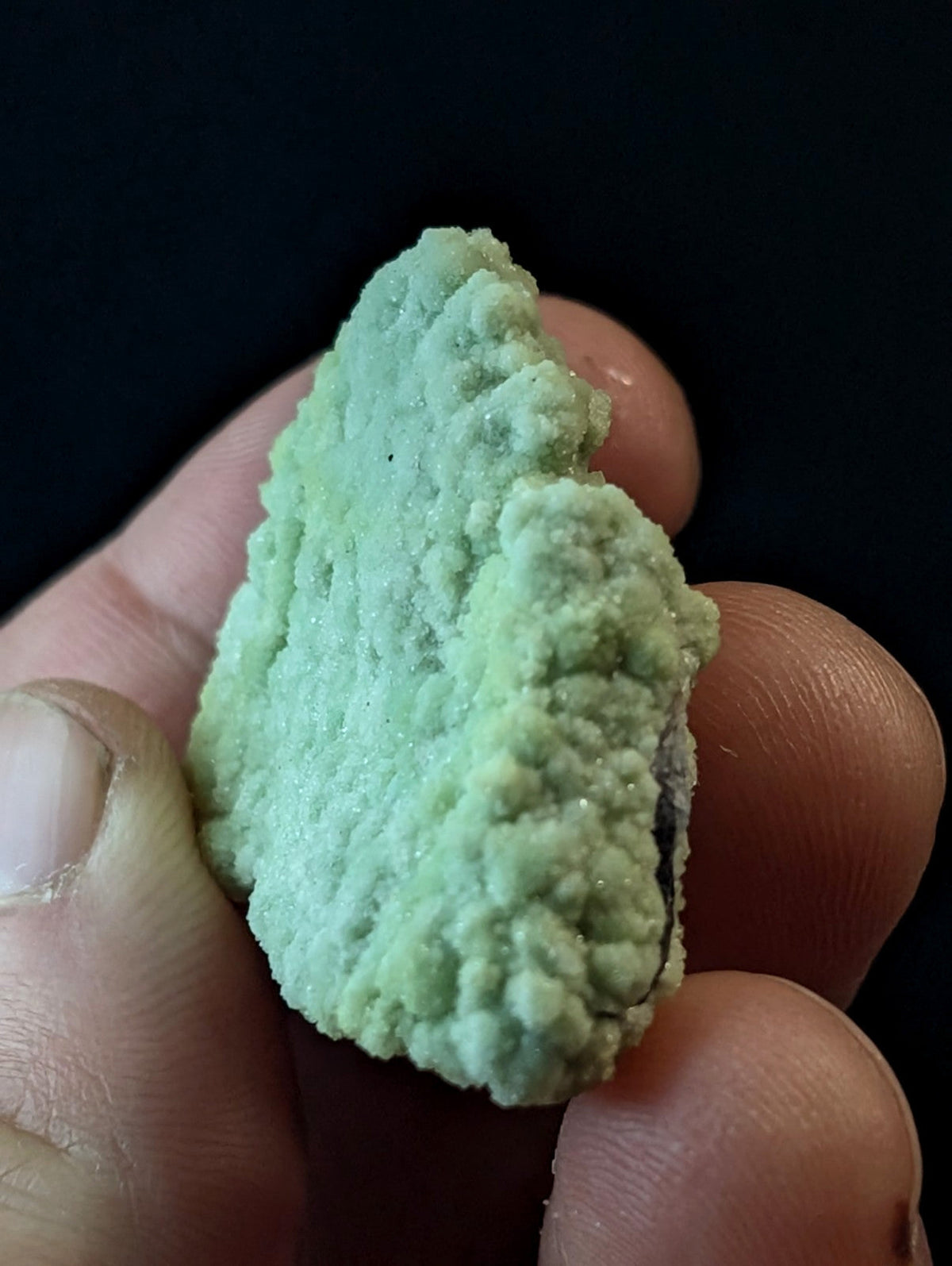 A pale green, textured mineral specimen with a rough, crystalline surface held in someone’s hand.