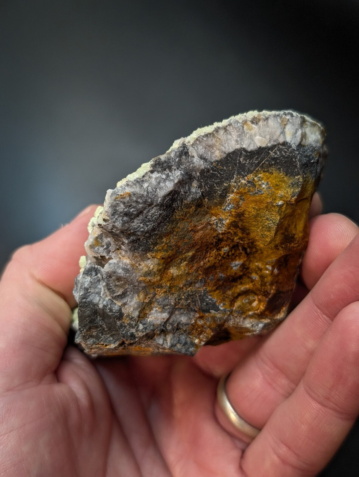 A rugged, naturally occurring mineral specimen with a striking patch of vibrant orange-yellow veining against a dark gray and white matrix.