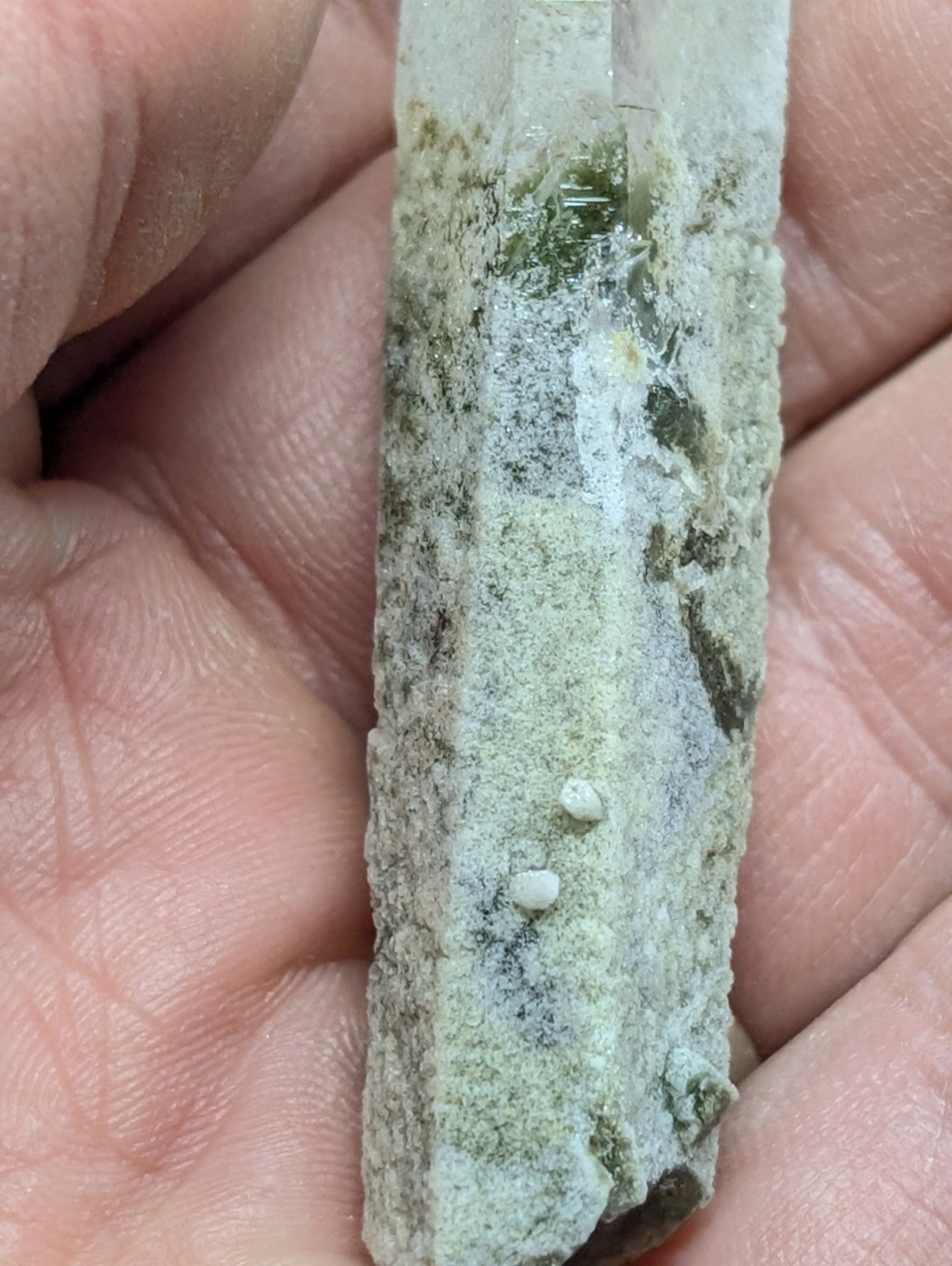 A weathered, translucent quartz crystal with green and white mineral inclusions.