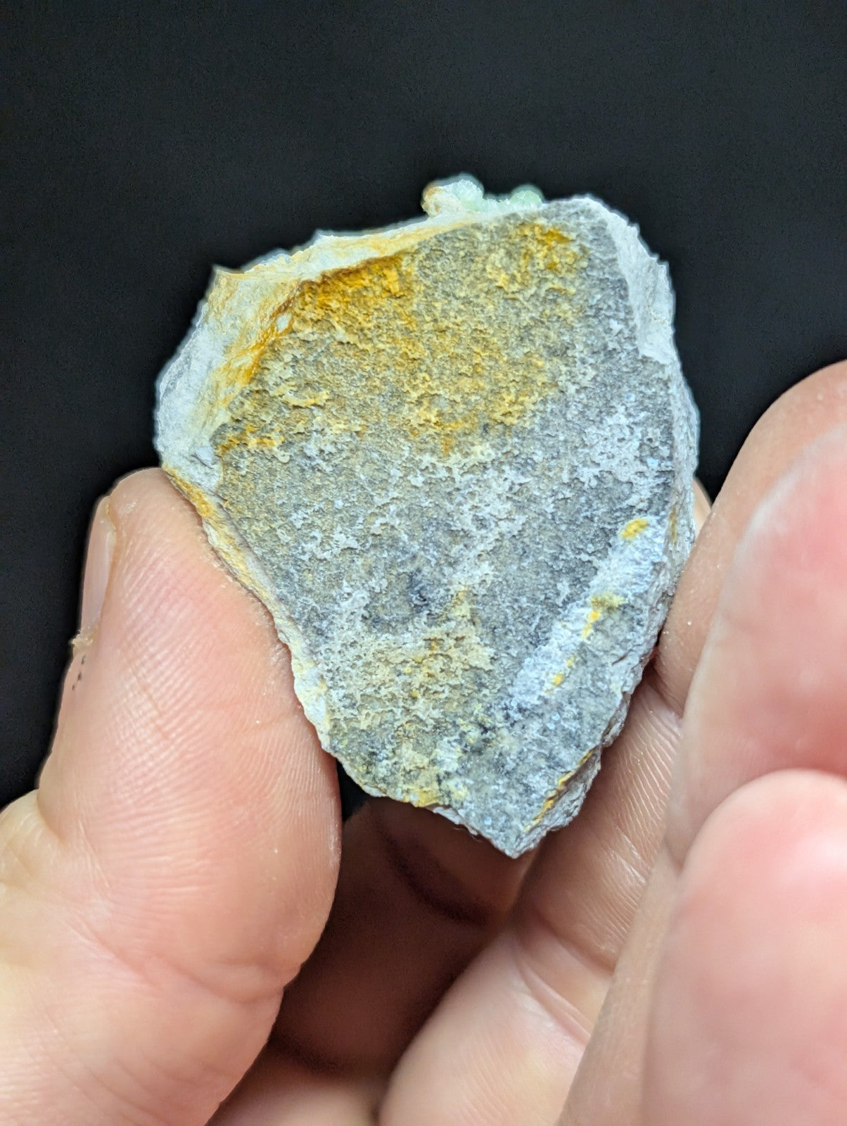 A rough, irregularly shaped stone with a gray base and patches of yellowish mineral streaks.
