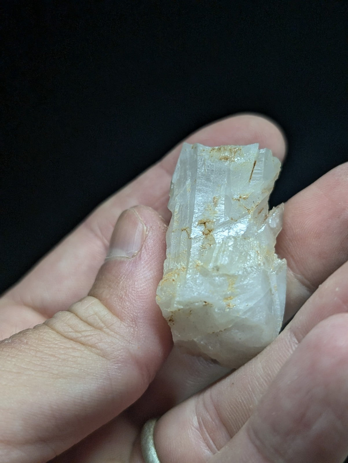 A translucent white mineral crystal with visible striations and faint golden inclusions, held gently in a person’s hand.