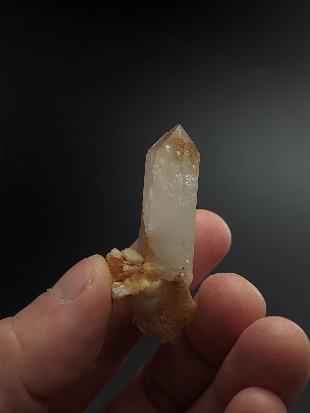 A translucent, pale quartz crystal with a pointed tip and earthy brown matrix base.