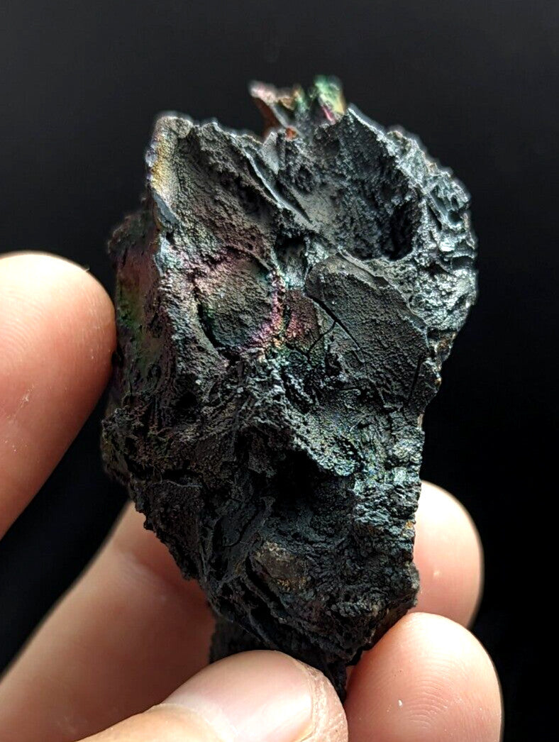 A rugged, dark green and black mineral specimen with iridescent patches of pink and purple hues.