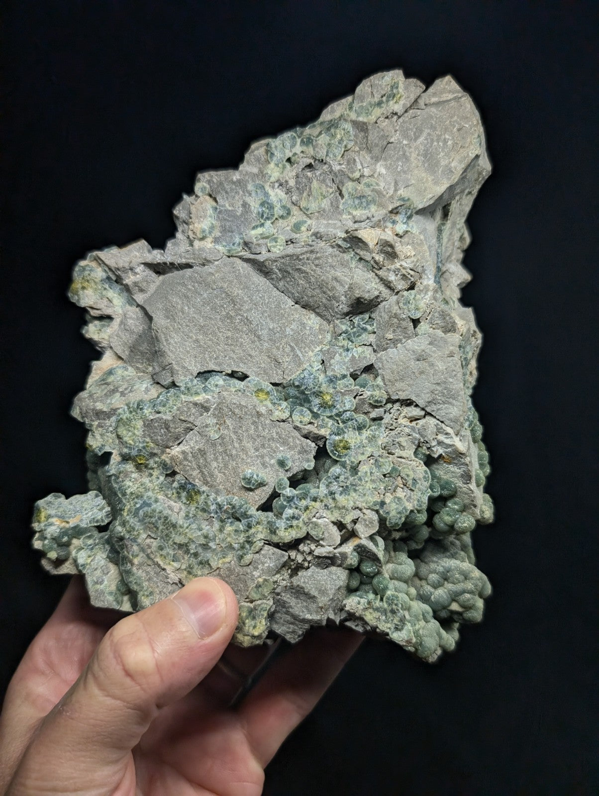 A rough, irregularly shaped mineral specimen with a grayish base and patches of green crystalline growths.