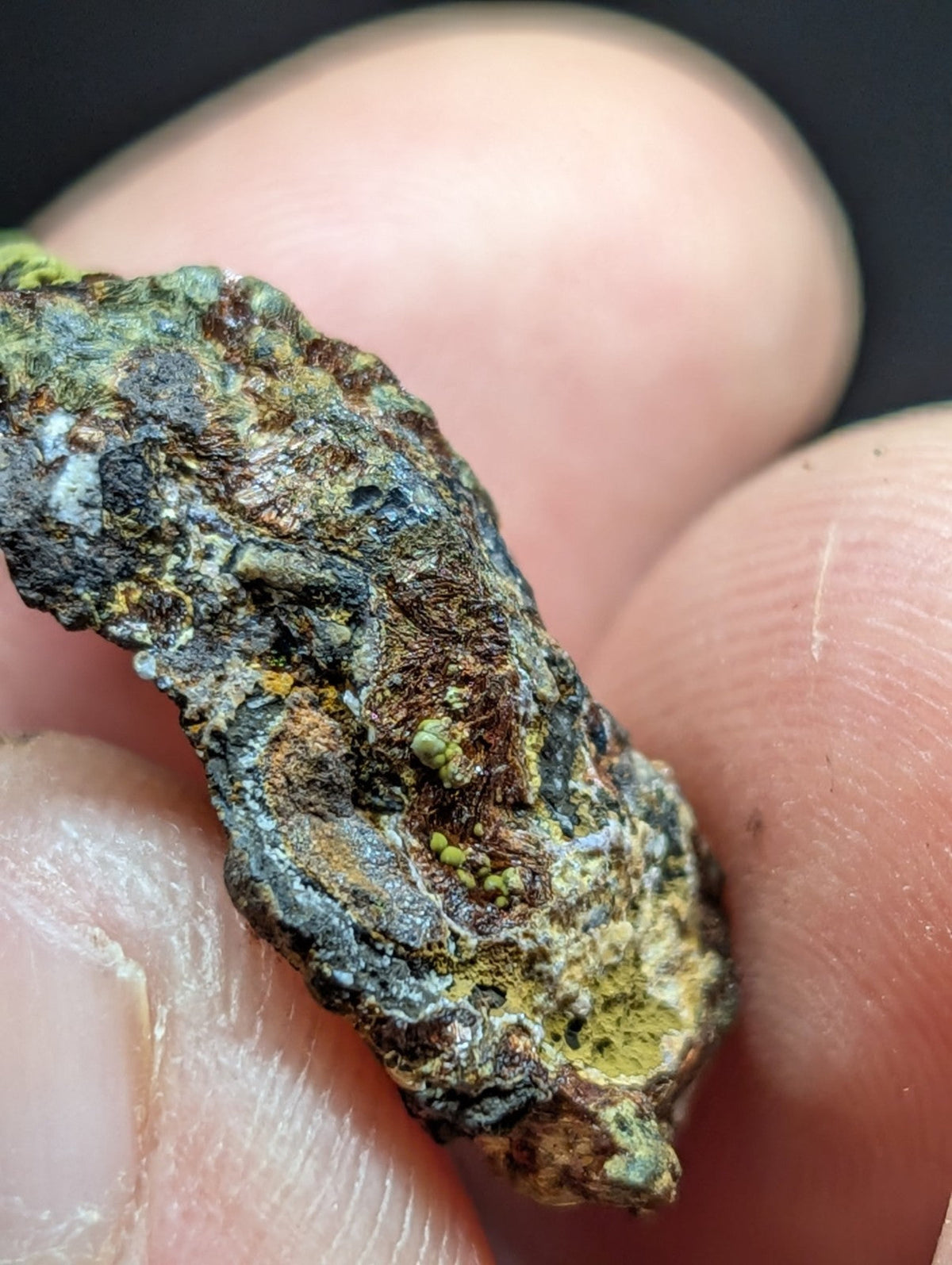 A rugged, irregularly shaped mineral specimen with a mottled surface of green, brown, and gray hues.