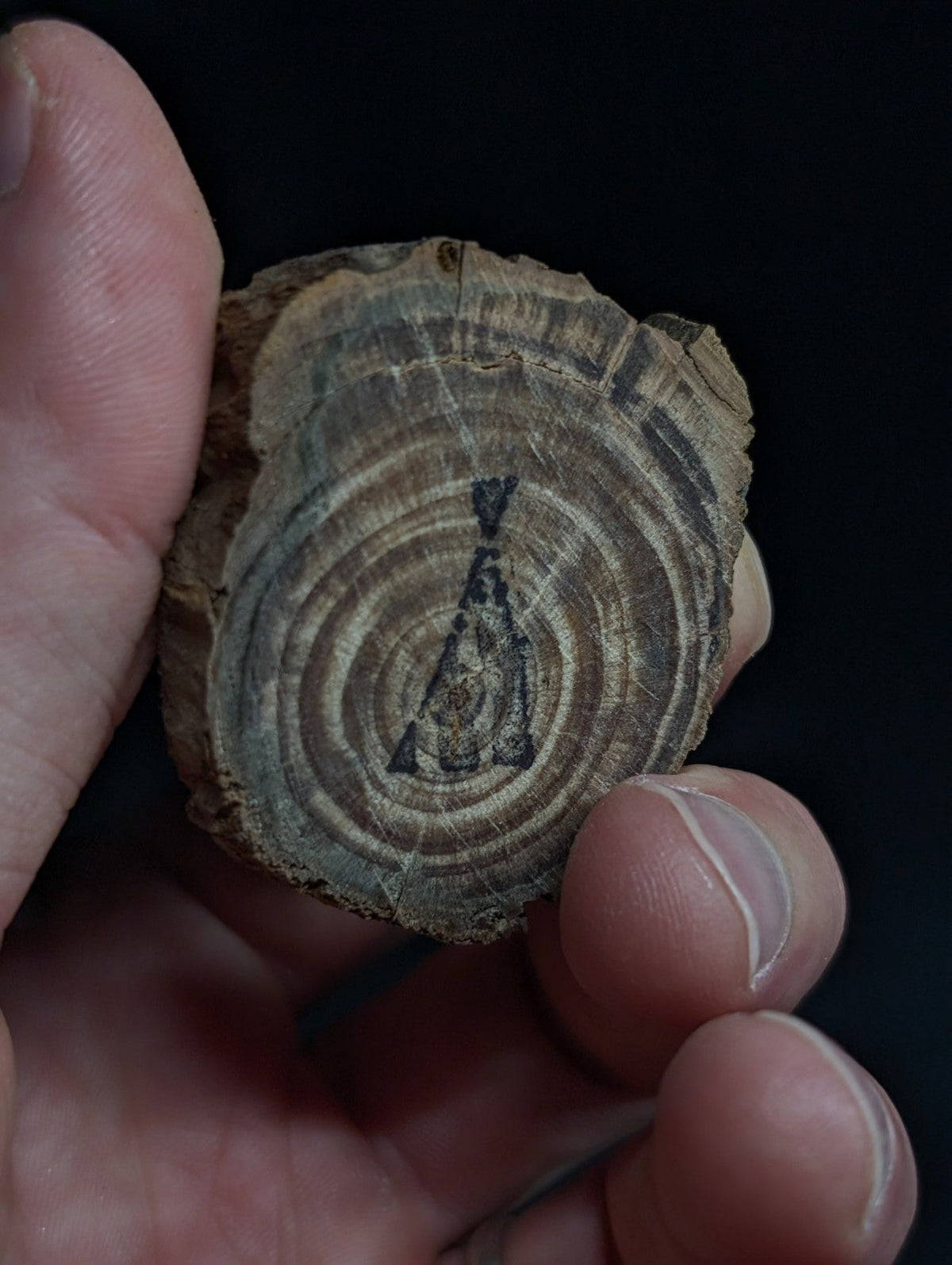 A rustic, circular wooden slice with visible growth rings and a dark engraved silhouette of a figure at its center.