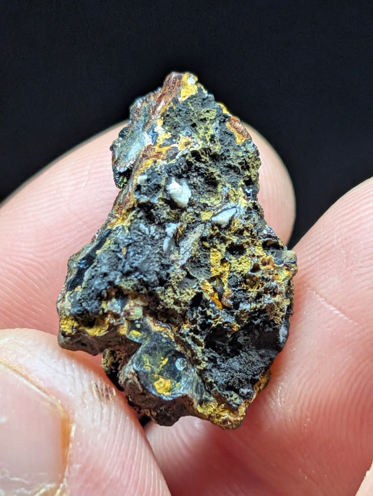 A rugged, irregularly shaped mineral specimen with a dark, textured surface accented by patches of vibrant yellow and subtle greenish-blue hues.