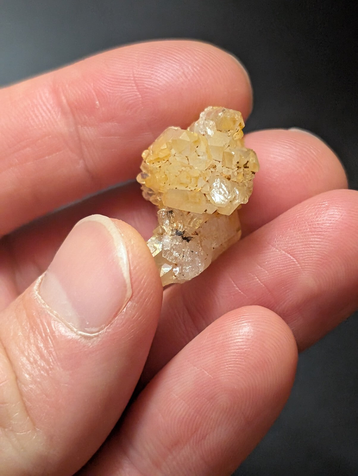 A translucent yellowish crystal cluster with a rough, faceted surface held gently in someone’s hand.