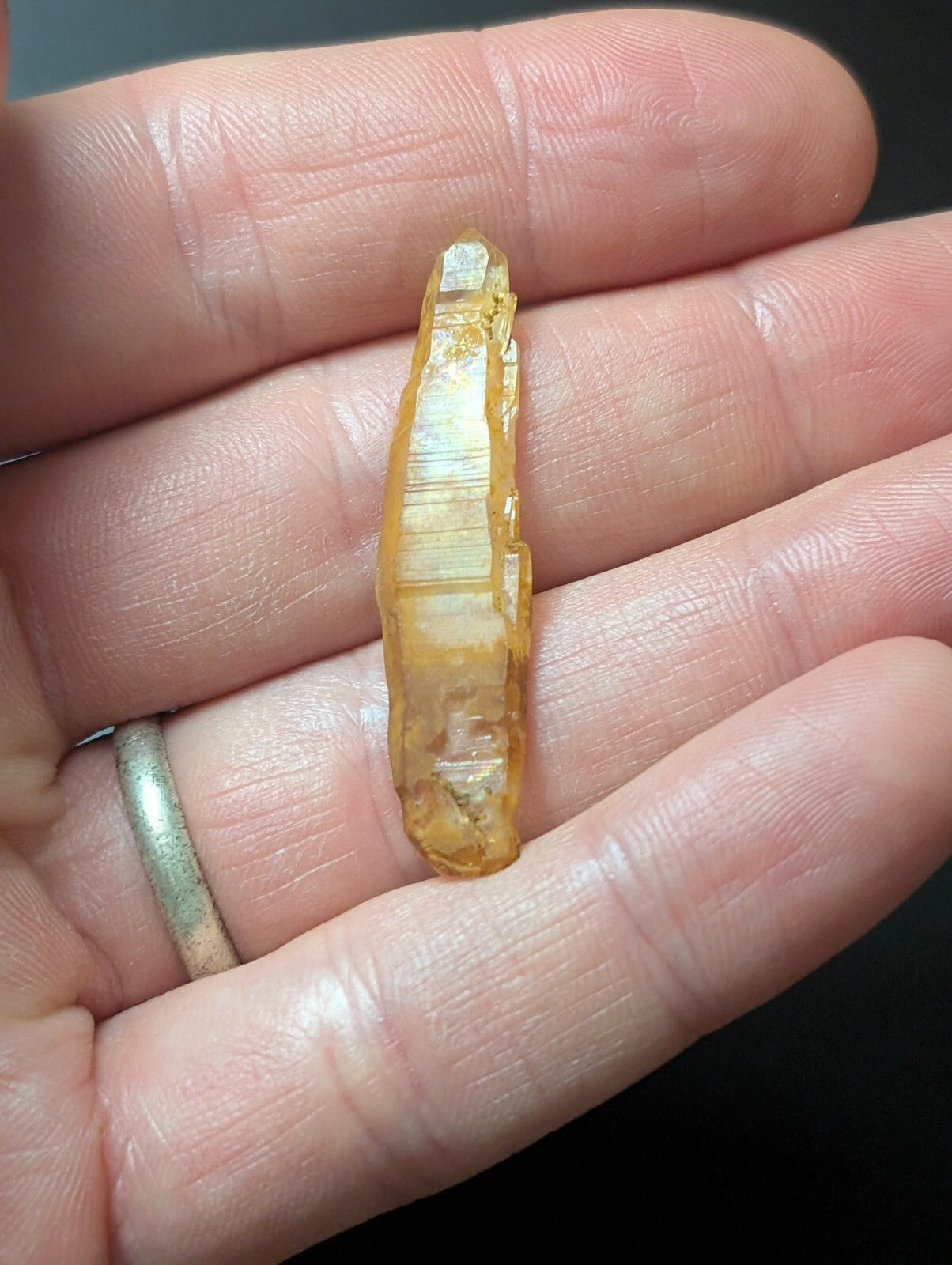 A translucent golden-yellow crystal with a pointed tip and visible internal striations, held gently in an open palm.