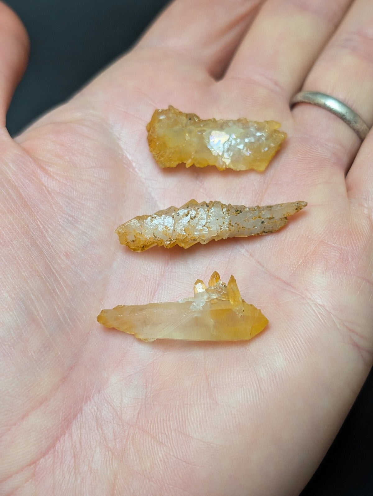 Three translucent yellow-orange crystal specimens with jagged, natural edges rest in an open palm.