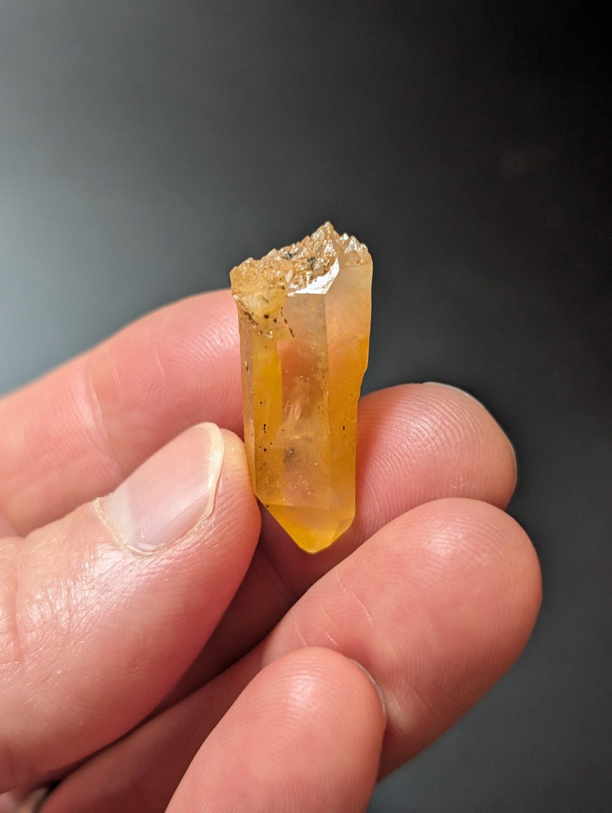 A translucent yellow-orange crystal with a rough, earthy top and smooth, faceted sides.