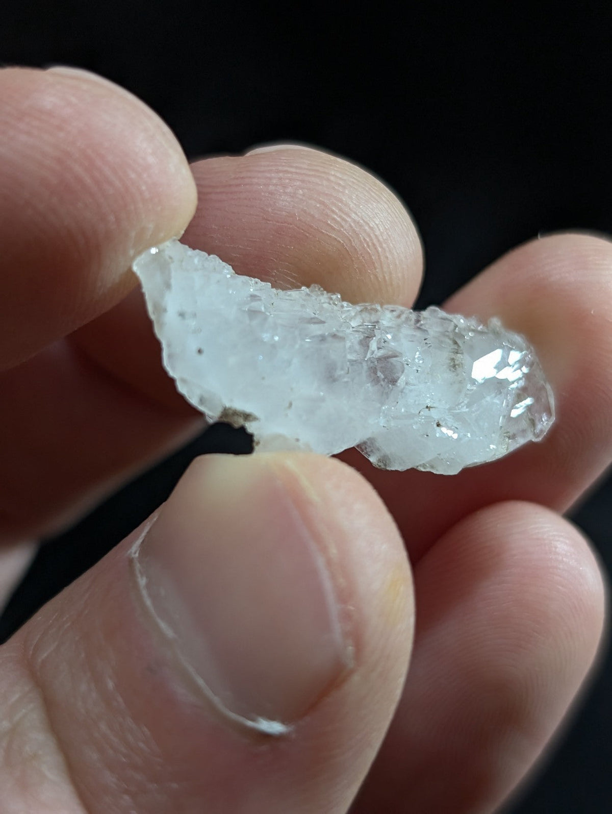 A translucent, irregularly shaped ice crystal fragment held between fingers.