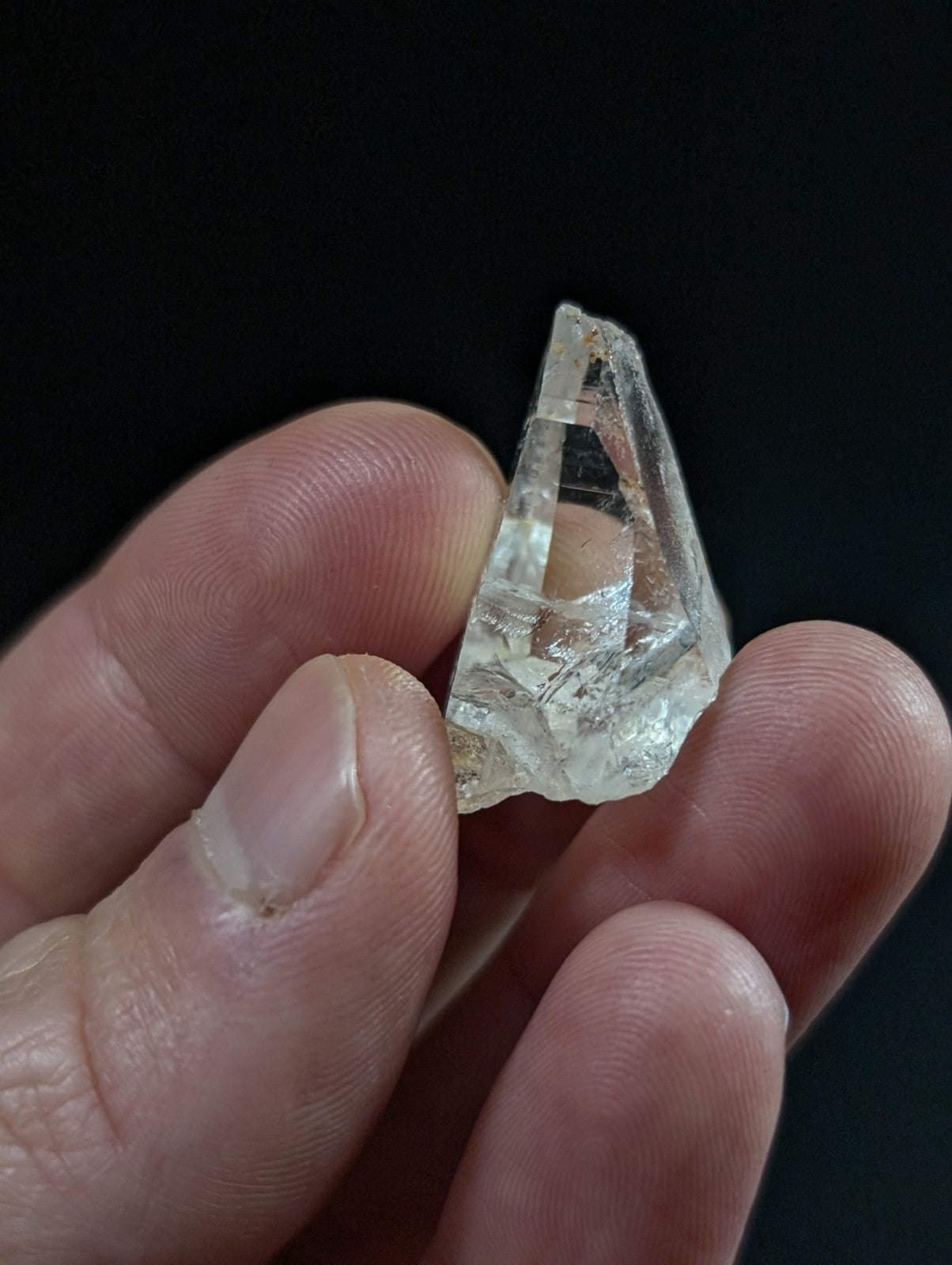 A clear, faceted quartz crystal fragment held between fingers.