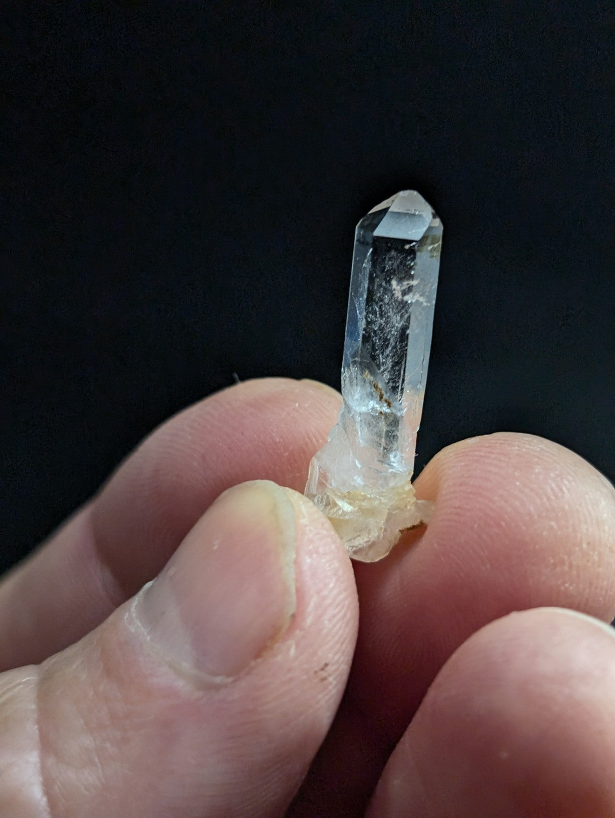A clear quartz crystal with a pointed tip and visible internal inclusions, held gently between fingers.