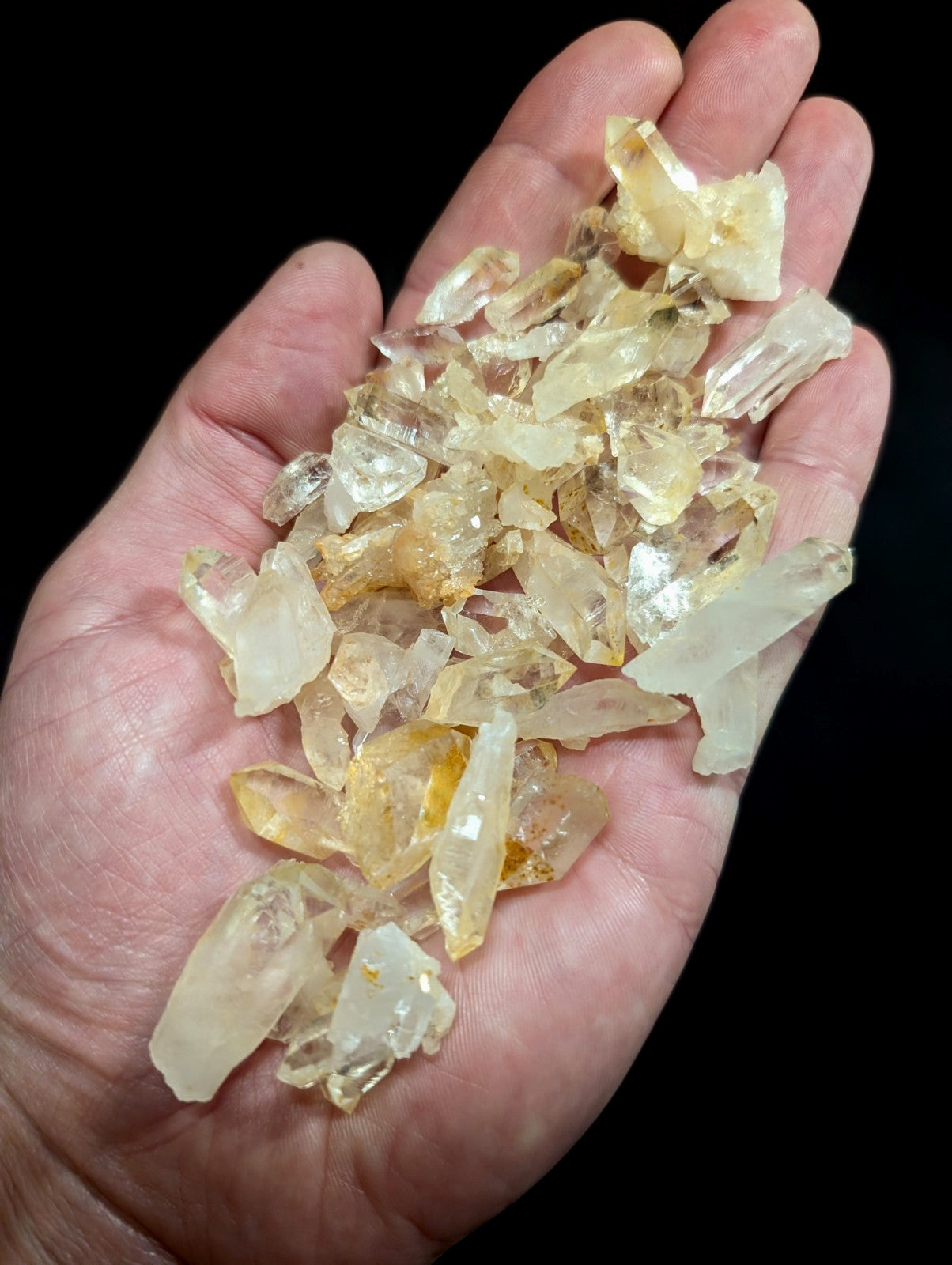 A hand holds a collection of translucent, pale yellow to clear quartz crystals with jagged edges and natural facets.