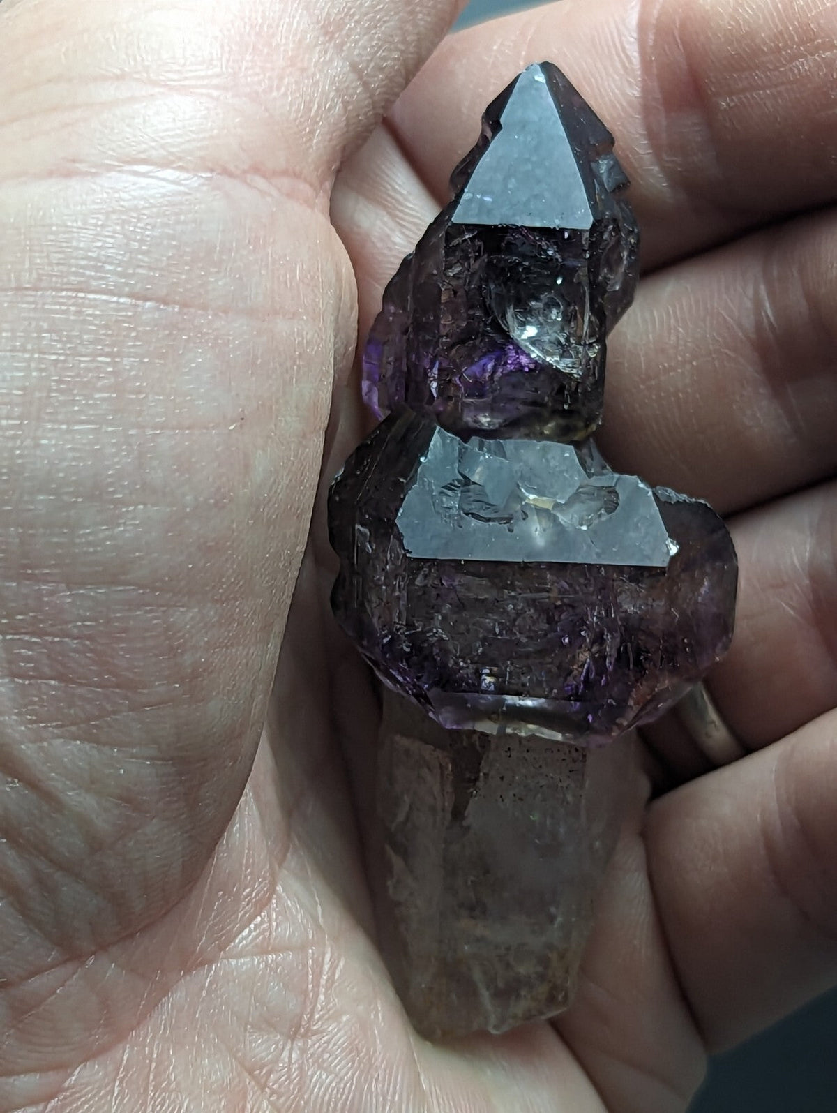 A hand holds a natural amethyst crystal cluster with deep purple and translucent sections, featuring sharp geometric facets.
