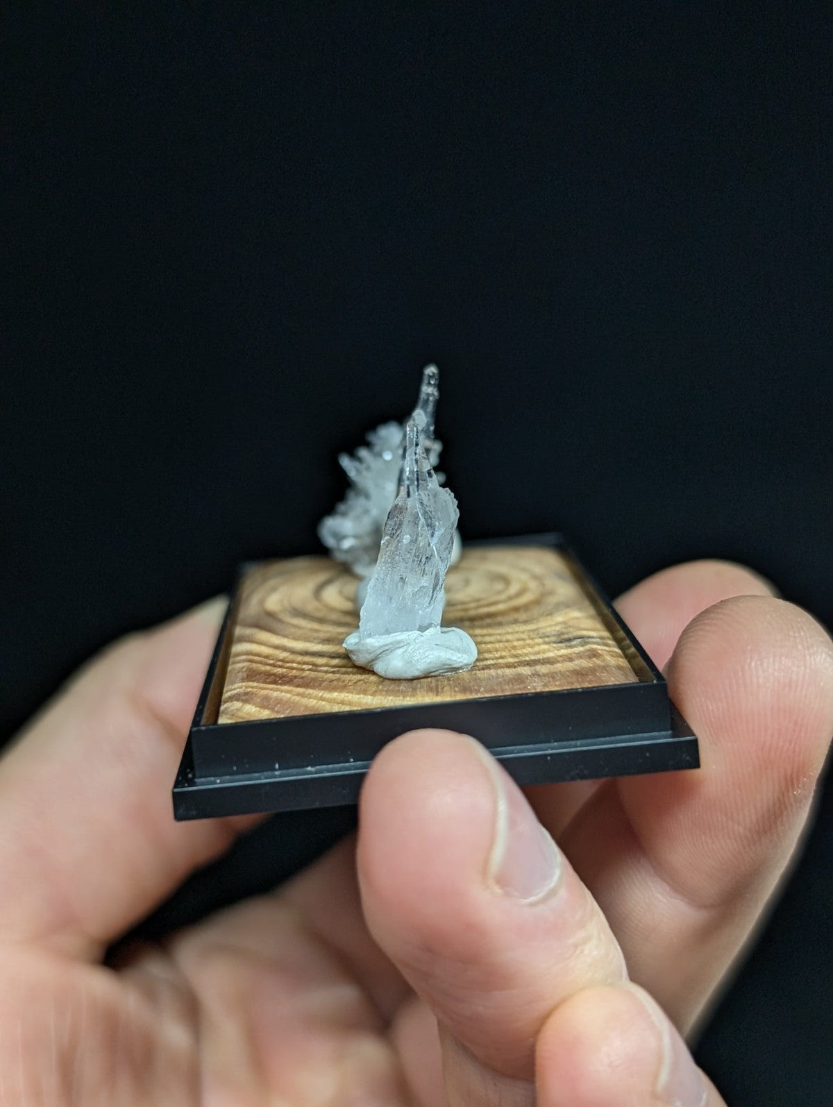 A translucent, crystalline mineral specimen with a jagged, natural formation rests on a wooden display base.