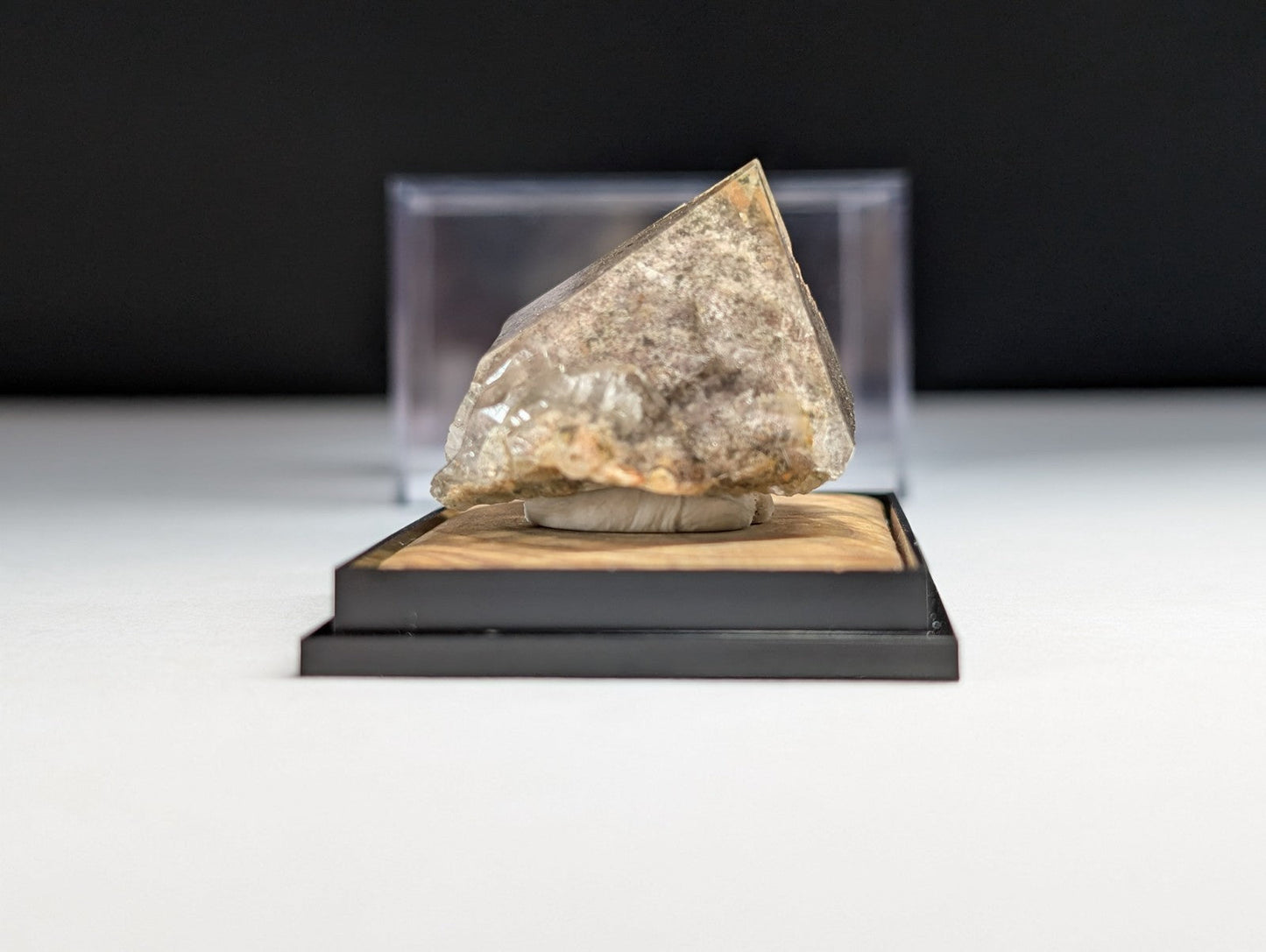 A translucent, triangular crystal specimen with a mottled gray and beige surface rests on a wooden display base.