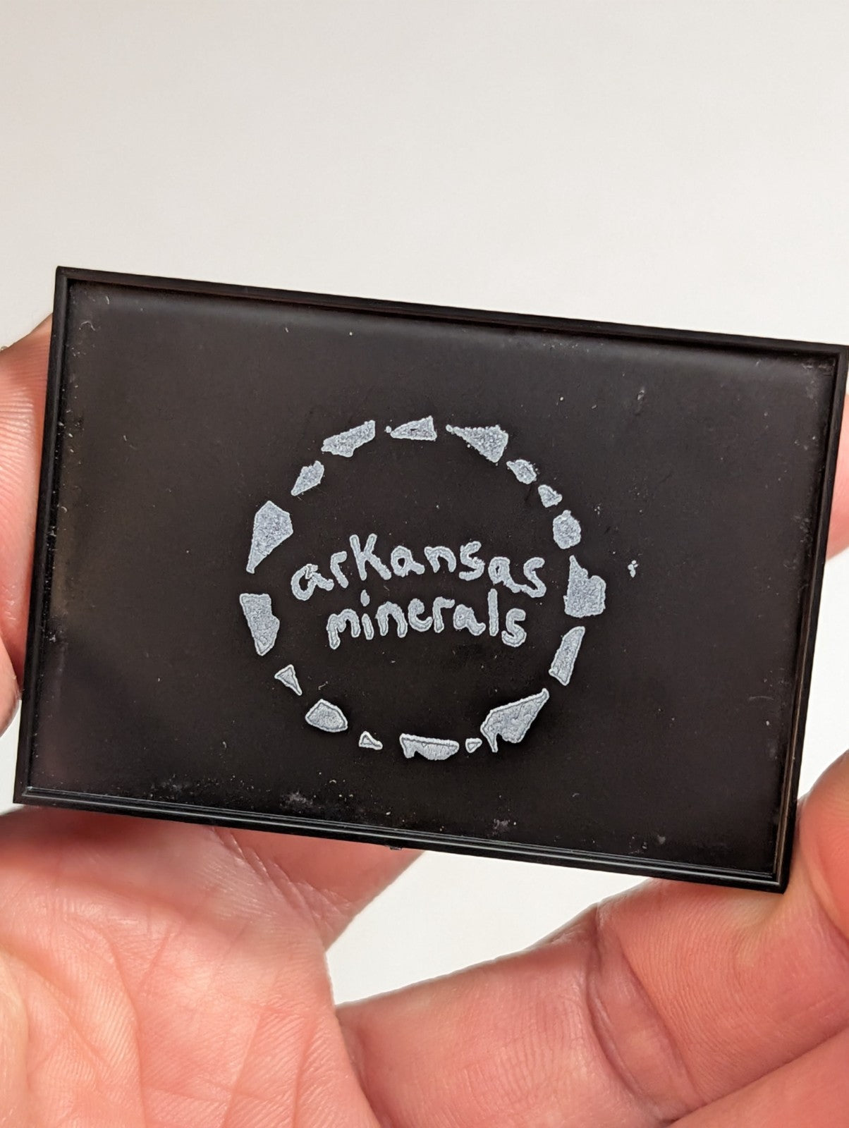 Black rectangular compact with silver glittery ’arkansas minerals’ logo encircled by a ring of sparkling mineral-shaped embellishments.