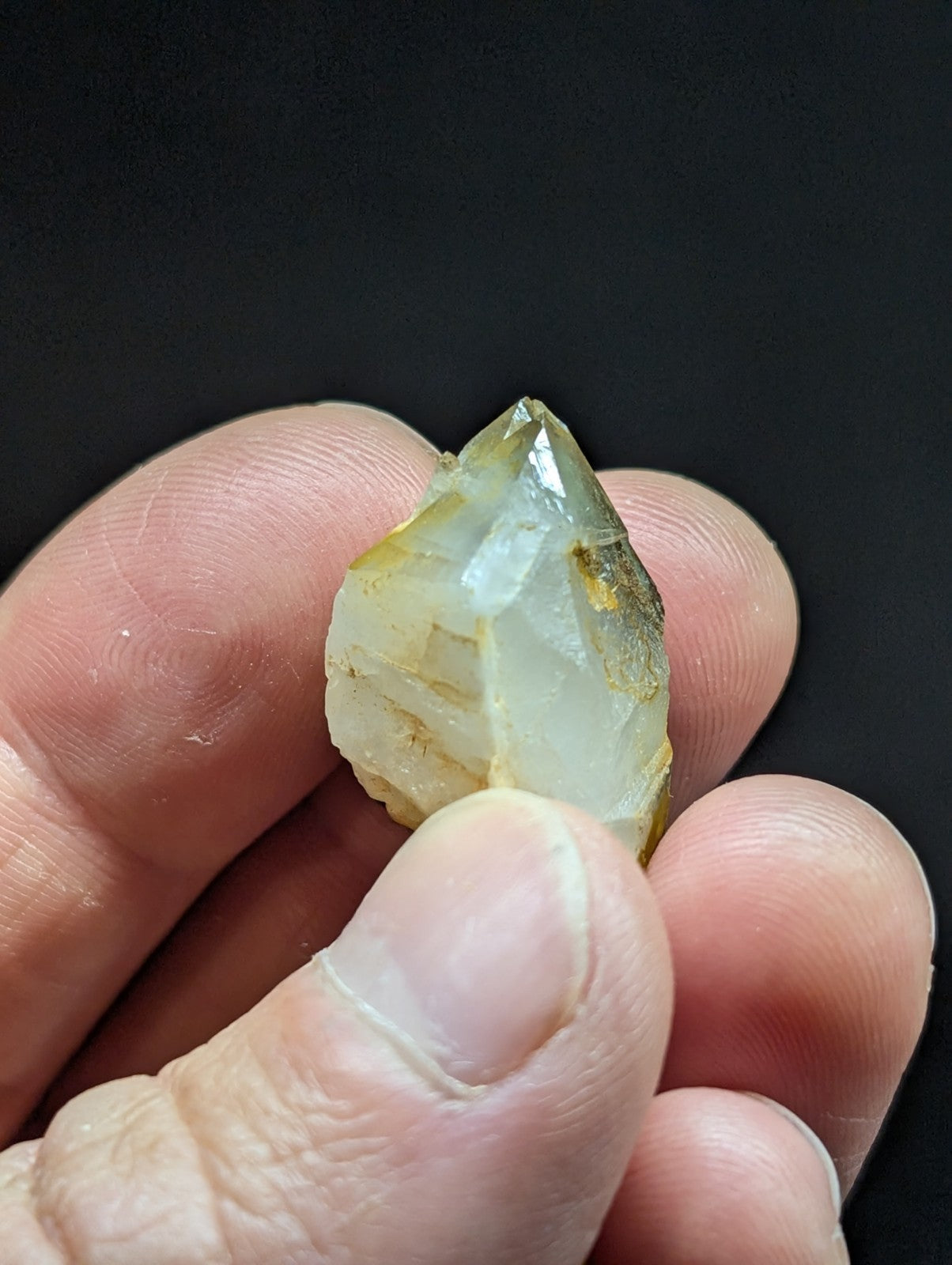 A translucent, pale yellowish-white quartz crystal with a pointed tip and visible internal inclusions.