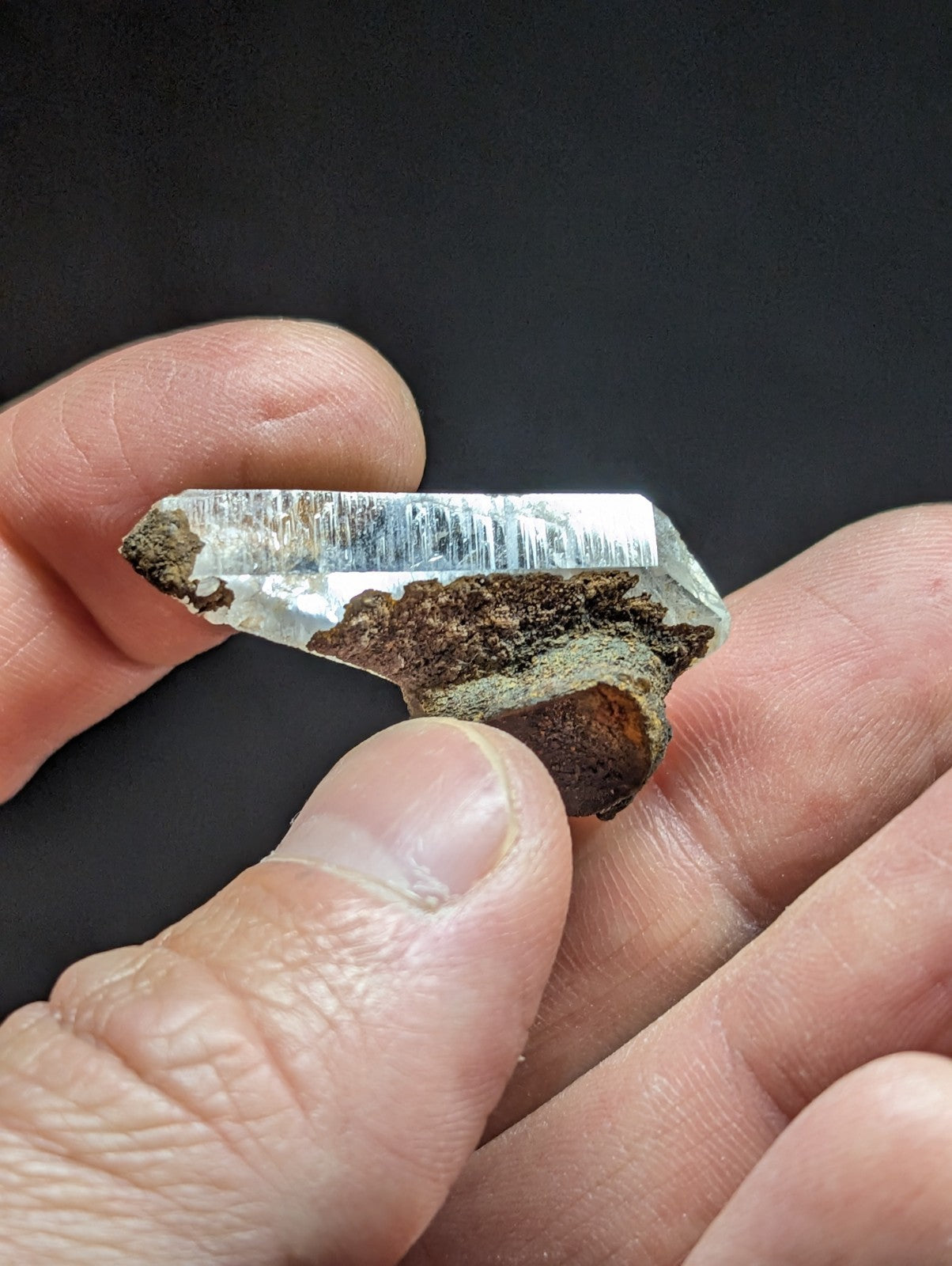 A clear quartz crystal with a rough, earthy brown base and sharp, faceted edges.