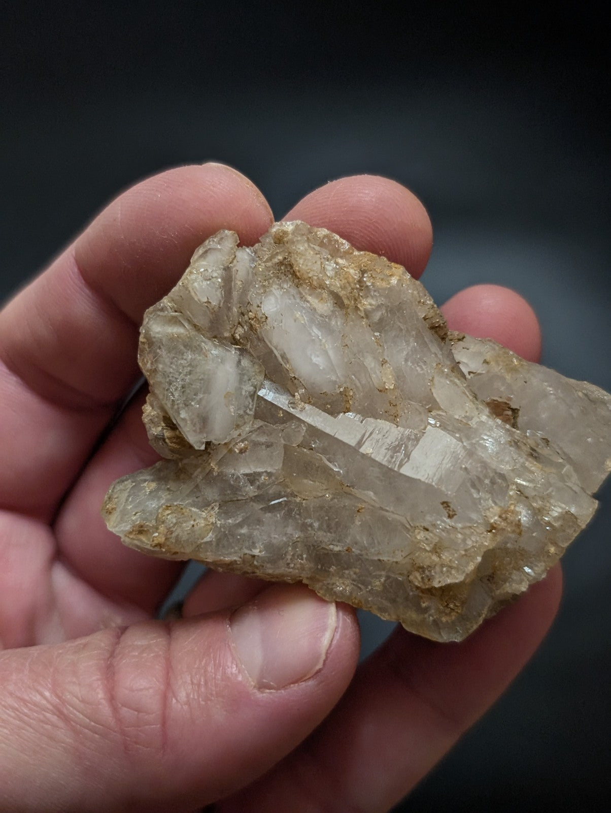A translucent, crystalline quartz cluster with golden-brown mineral inclusions held gently in a hand.