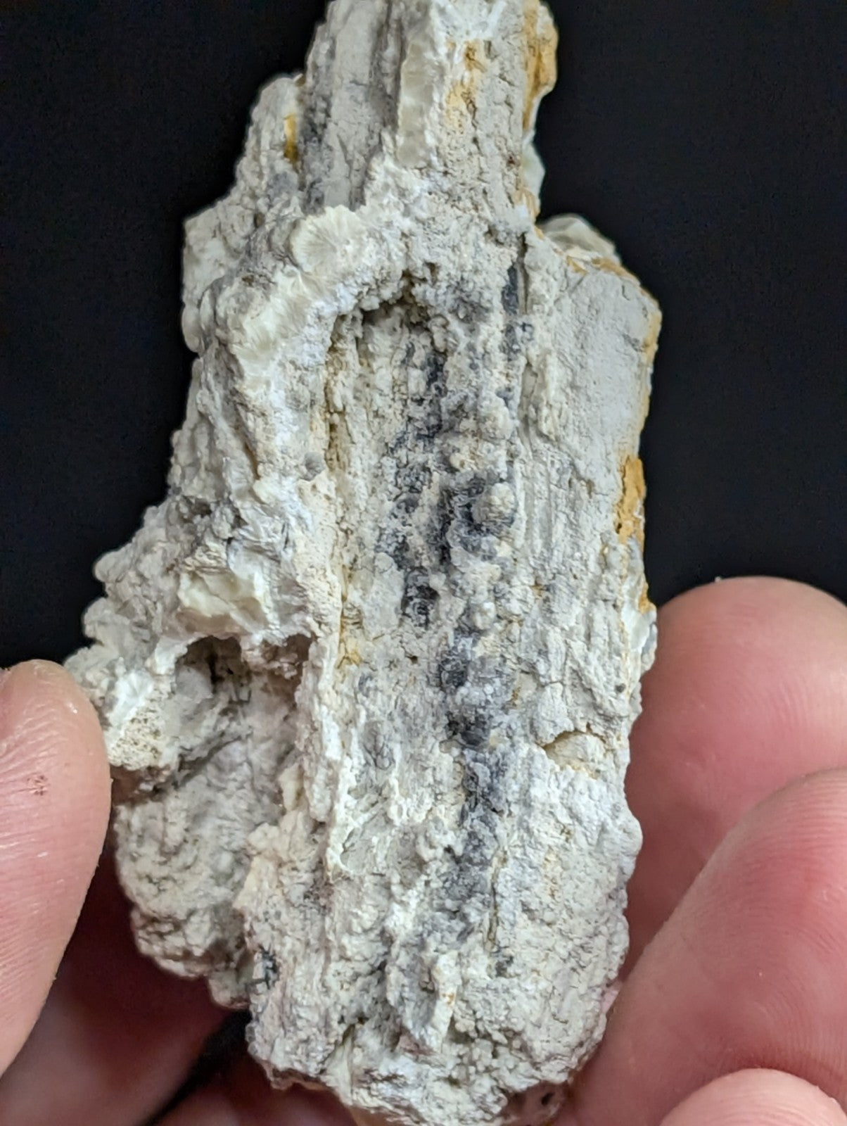A rough, irregularly shaped mineral specimen with a predominantly white and gray surface, accented by patches of yellowish discoloration.