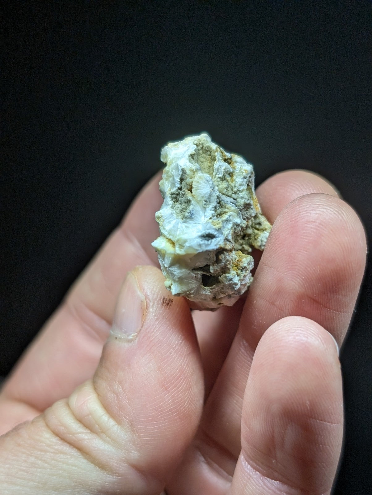 A rough, irregularly shaped mineral specimen with a pale white base and patches of yellowish-green veining.