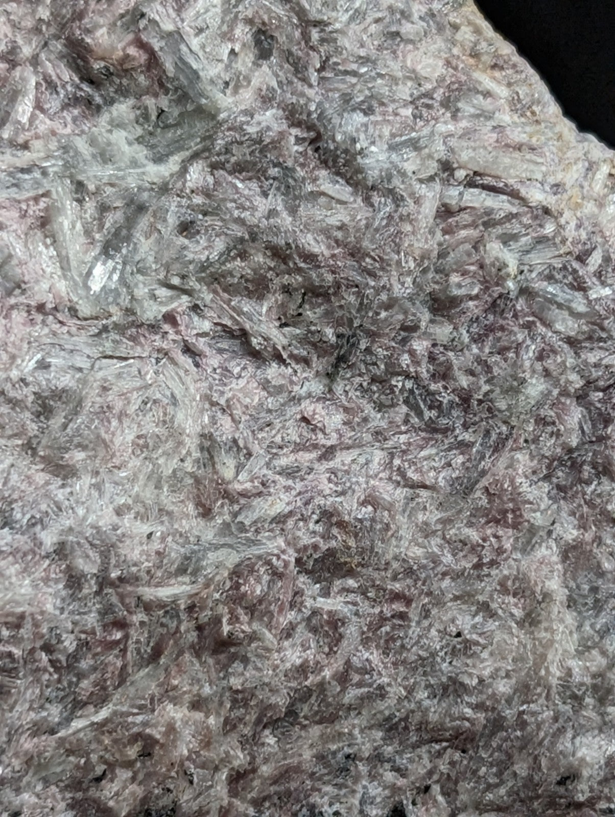 A rough, naturally occurring mineral specimen with a mottled gray and pinkish hue featuring translucent crystalline structures embedded in a darker matrix.