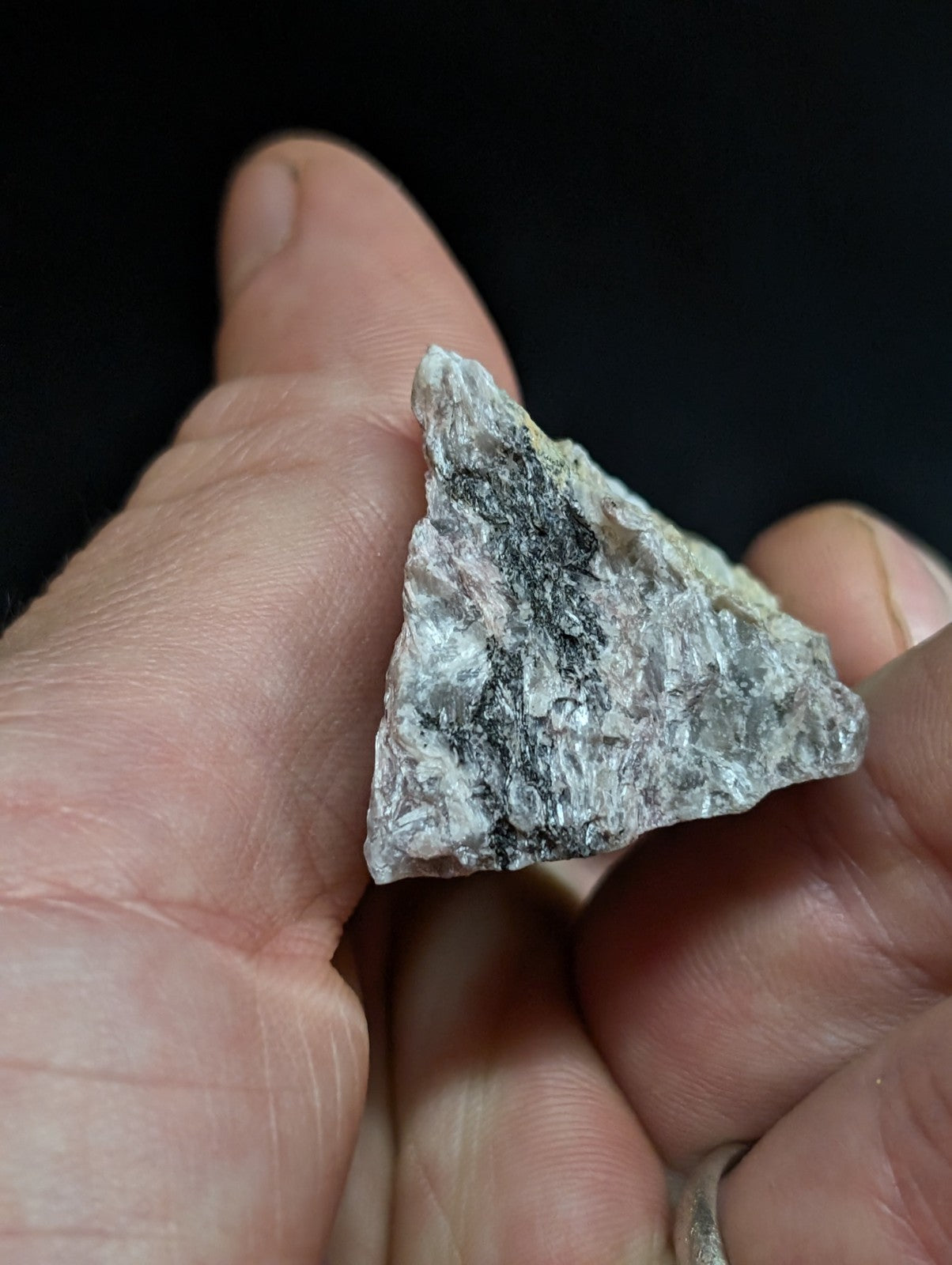 A rough, triangular piece of grayish-white rock with dark speckles and a textured surface.