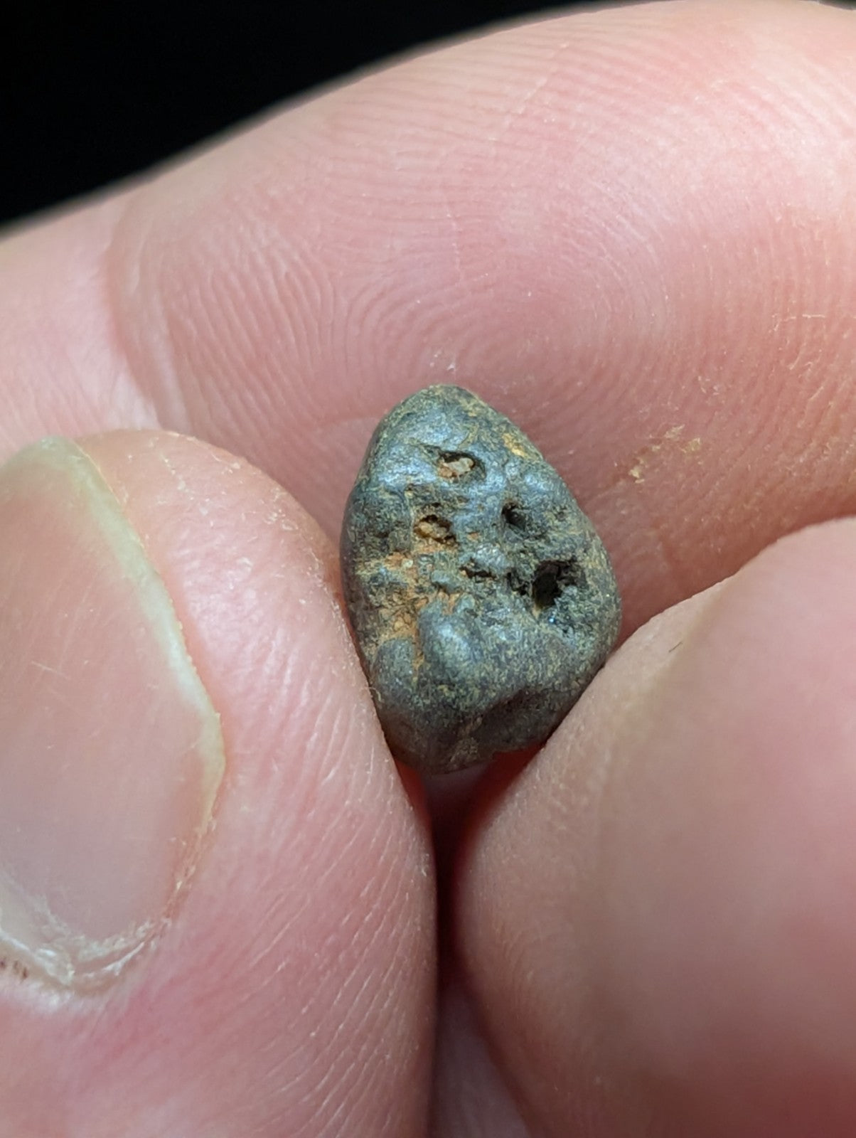 A small, weathered greenish-gray metallic object with a rough, irregular surface and visible pits.