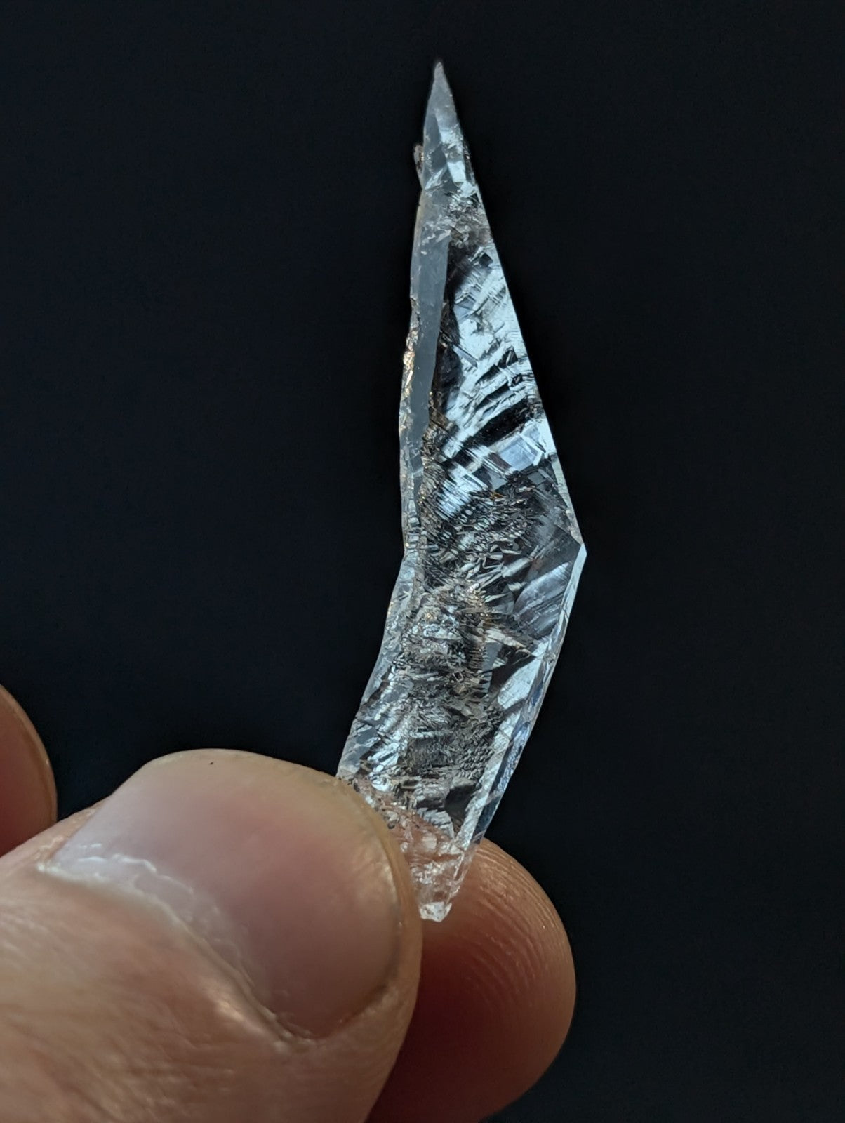 A clear, faceted quartz crystal with a pointed tip and intricate internal striations.