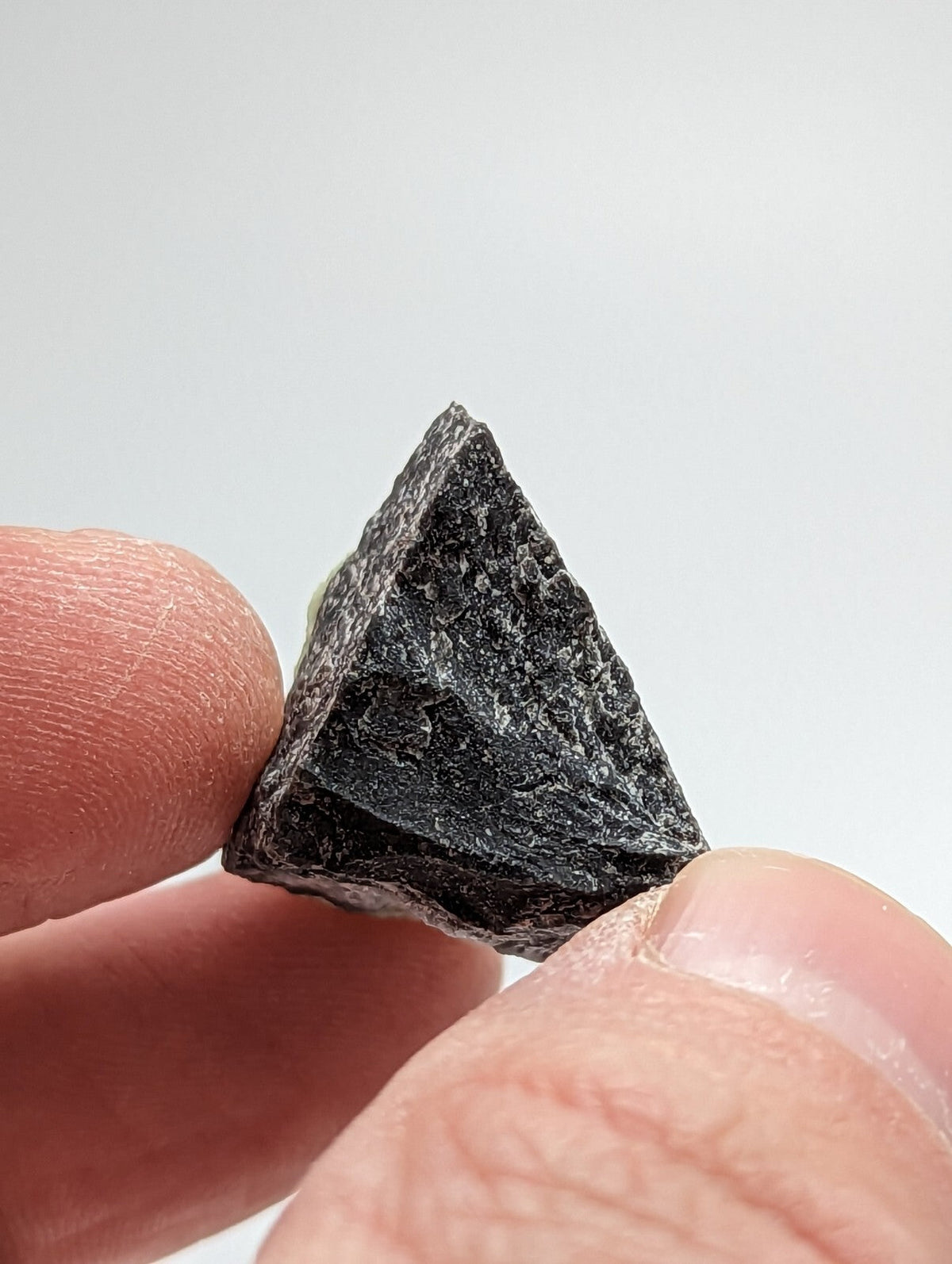 A dark, rough-textured triangular rock held between fingers.