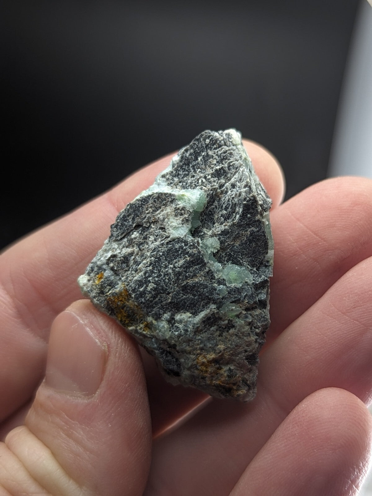 A rough, irregularly shaped mineral specimen with a mottled surface of dark gray and light green patches.