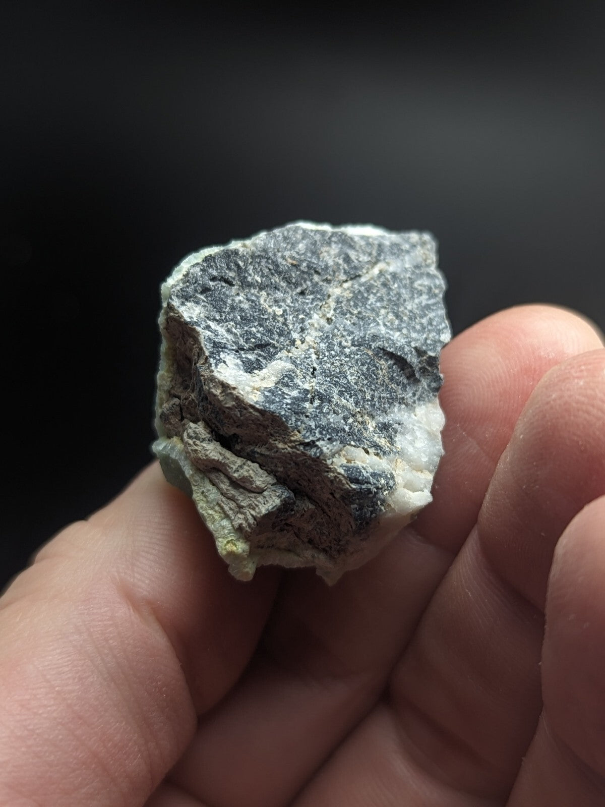 A rough, irregularly shaped mineral specimen with a mottled gray and white surface held in someone’s hand.